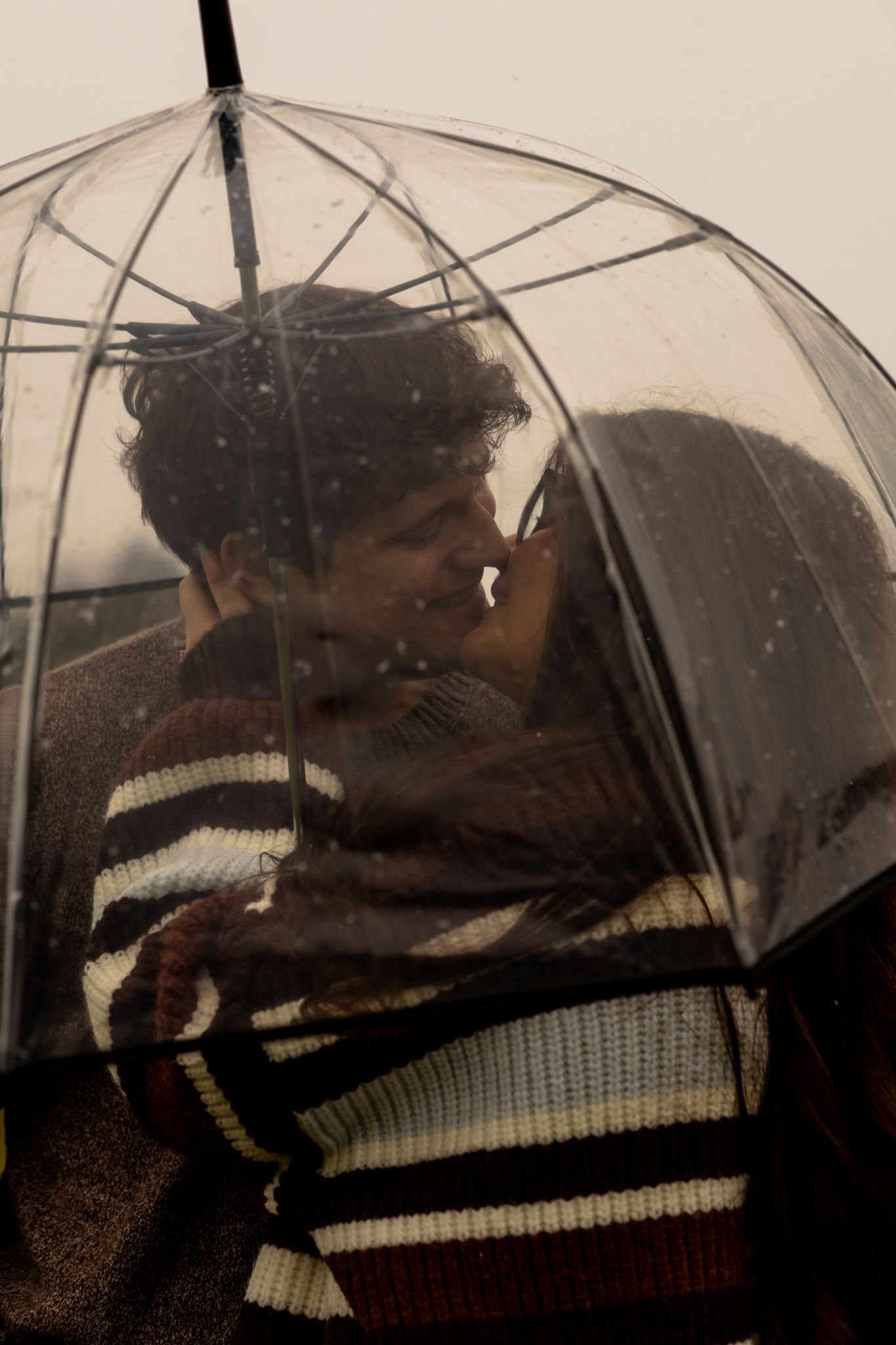 A romantic moment captured under a clear umbrella during snowfall.
