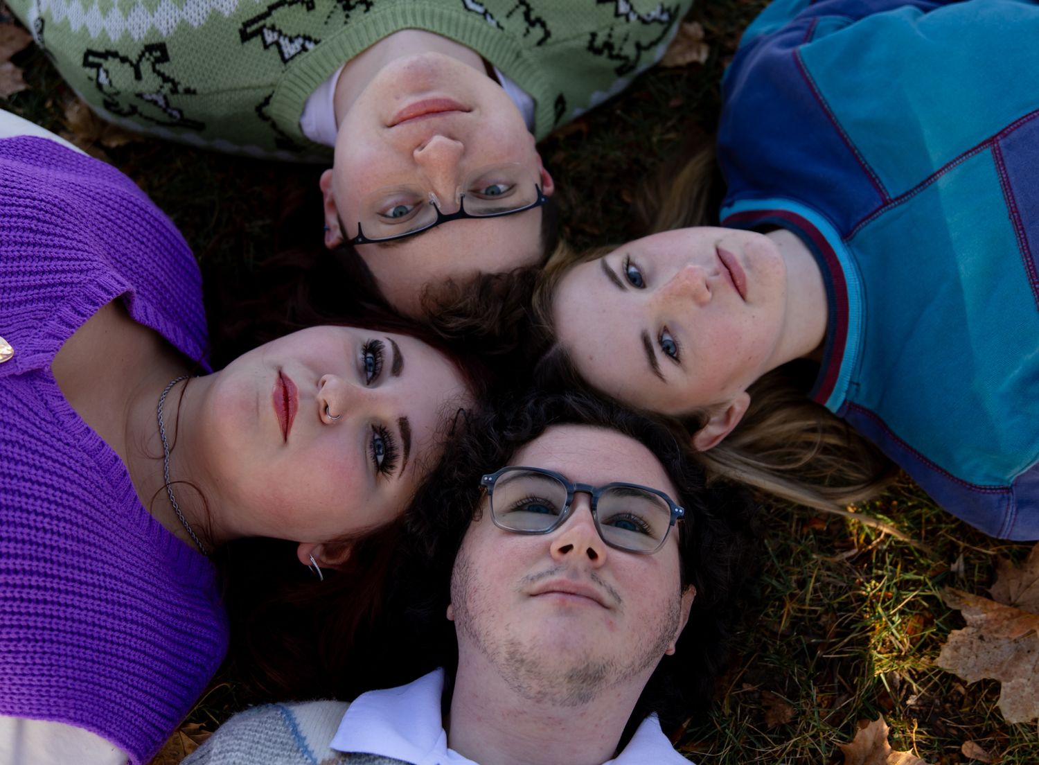 Friends lying on autumn leaves wearing casual clothes and sharing relaxed moments.