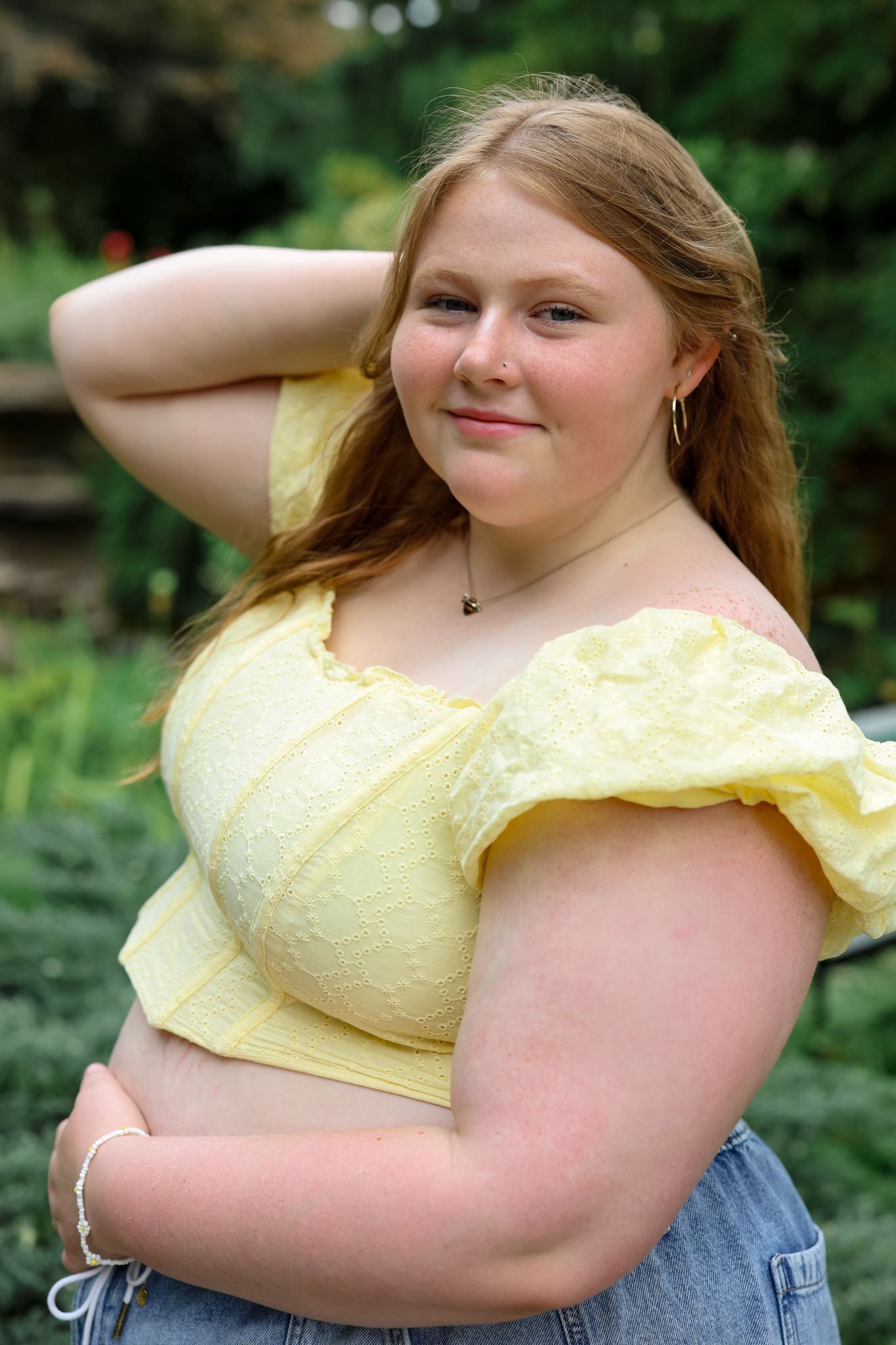 Person in yellow top posing playfully against natural outdoor background.