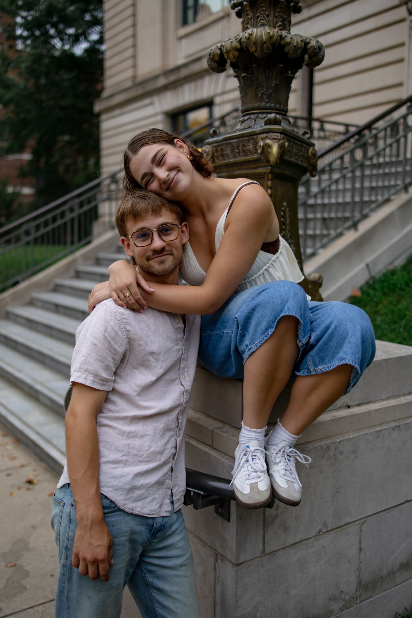 A couple shares a playful moment on stone steps outside a historic building.