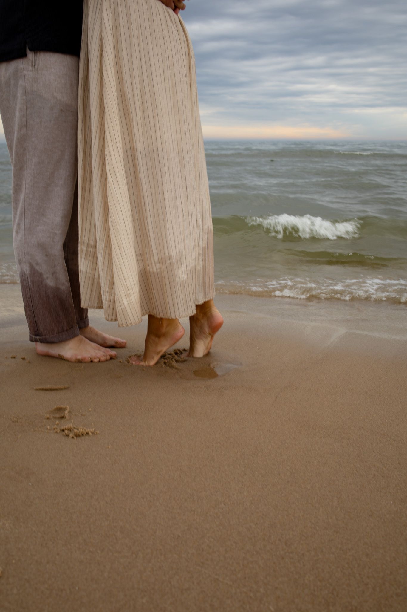 Bare feet of a couple standing close together on wet beach sand.