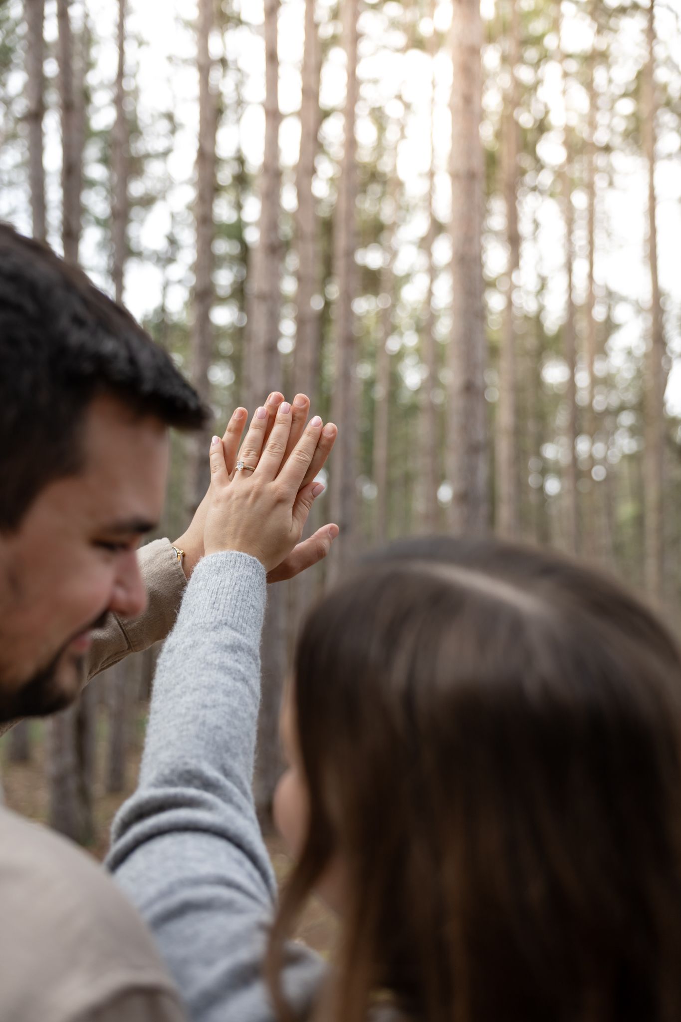 Couple sharing a high five in a sunlit forest, with tall pine trees in the blurred background.