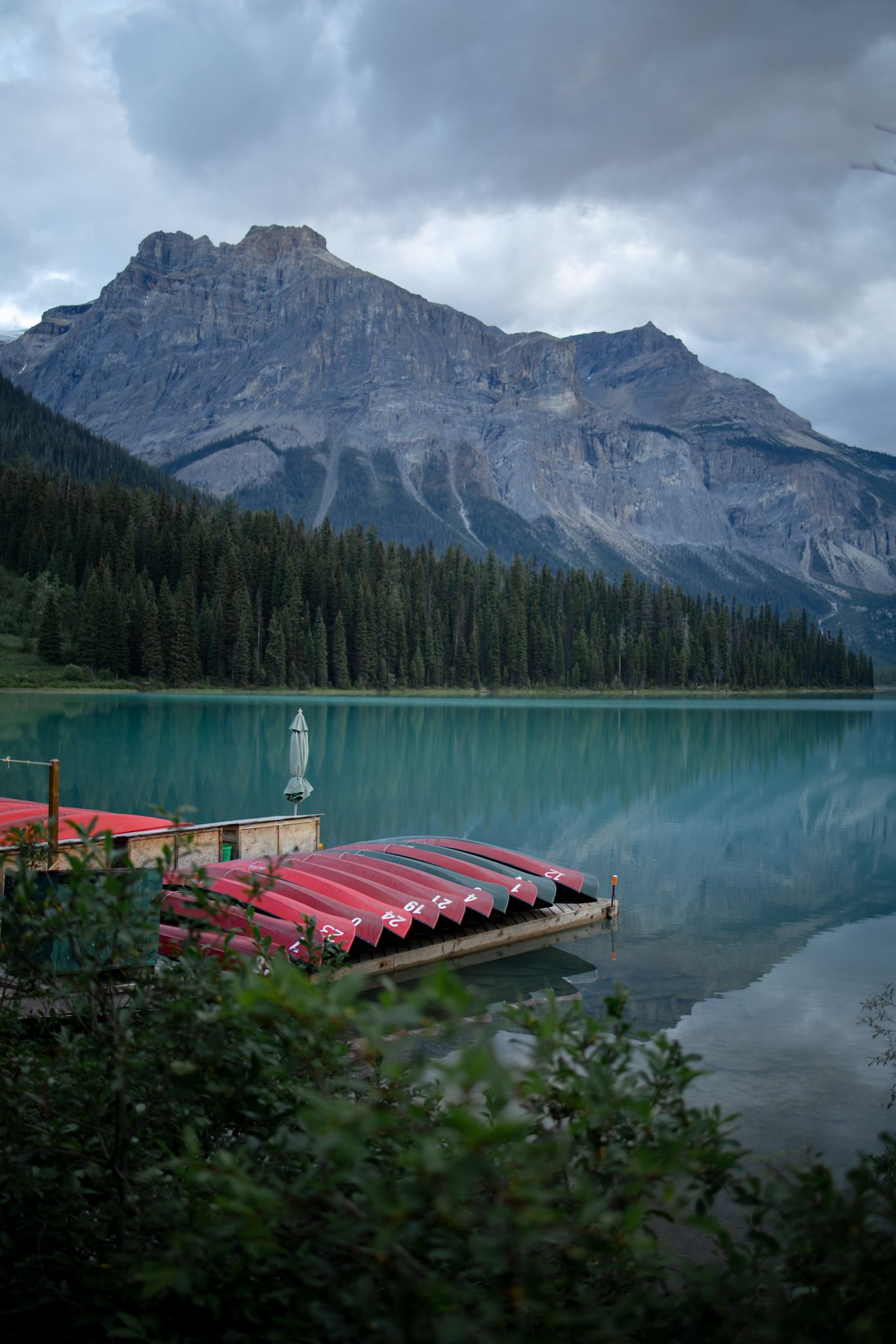 Red canoes docked on a tranquil emerald lake with mountain backdrop.