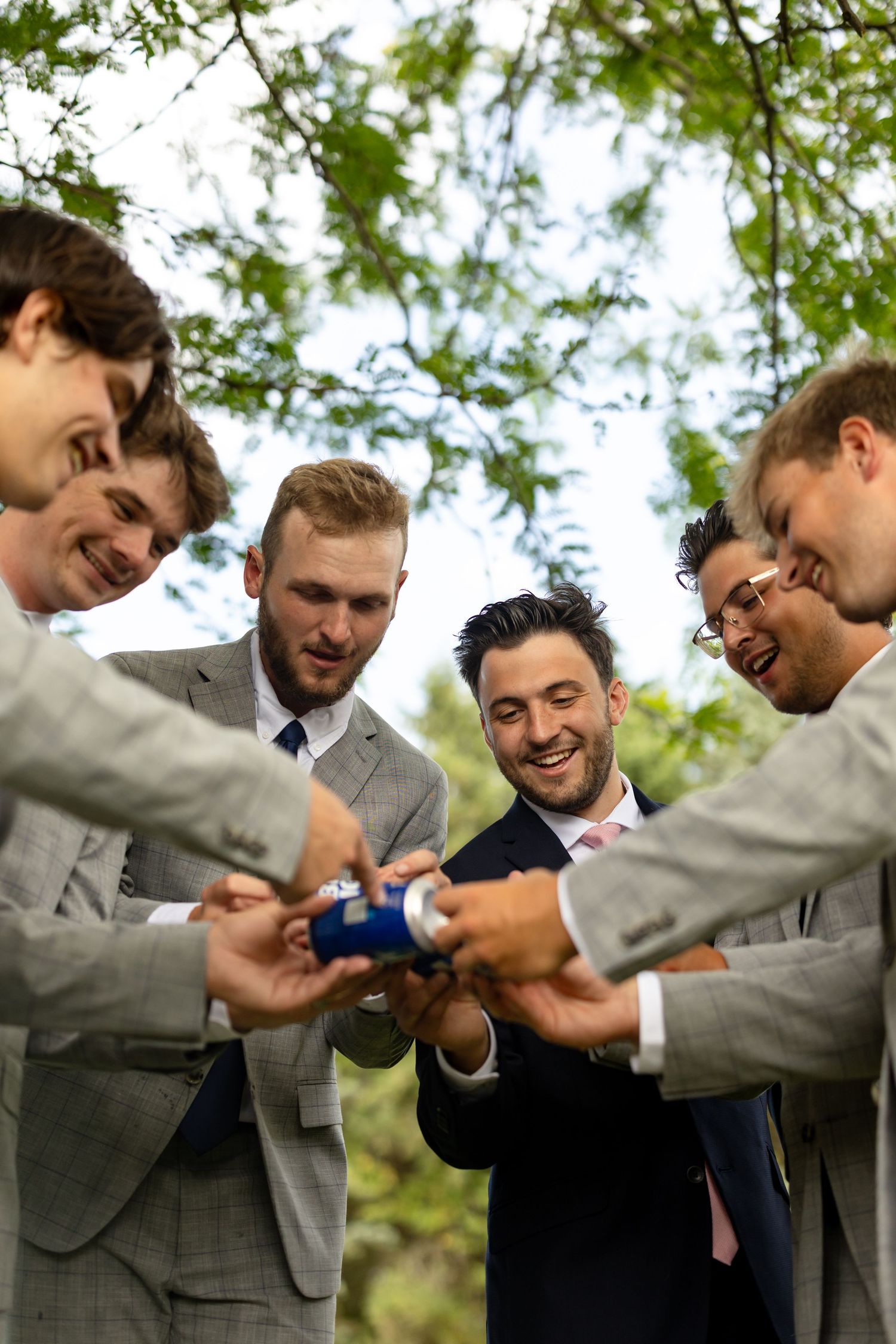 Groomsmen in gray suits looking at something on their phones together.