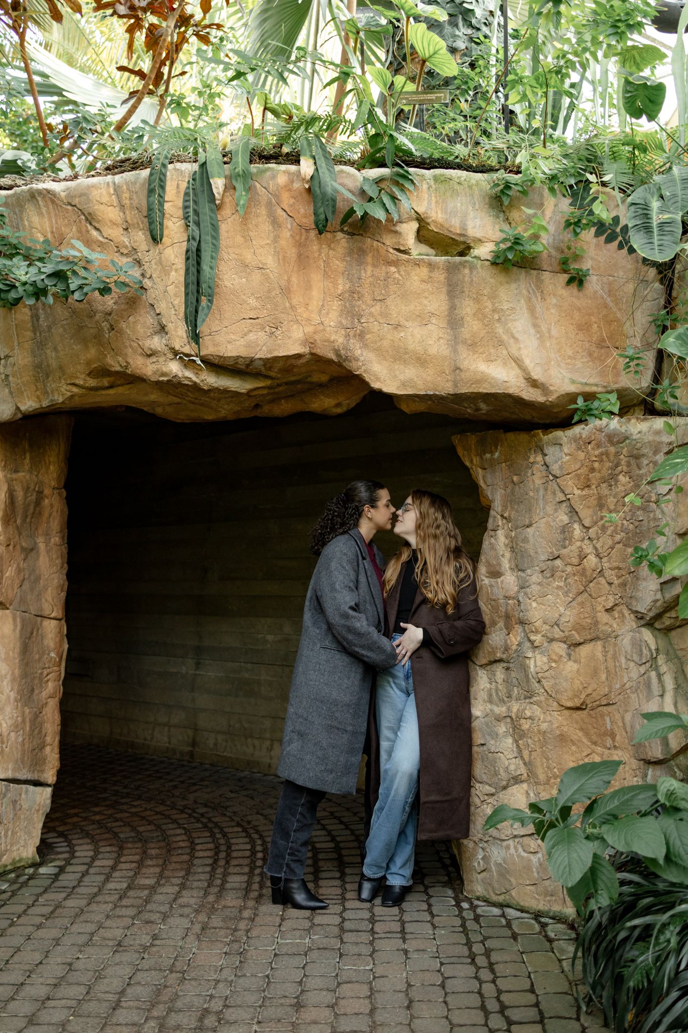 A romantic moment captured in a stone archway surrounded by lush greenery and brick pavement.