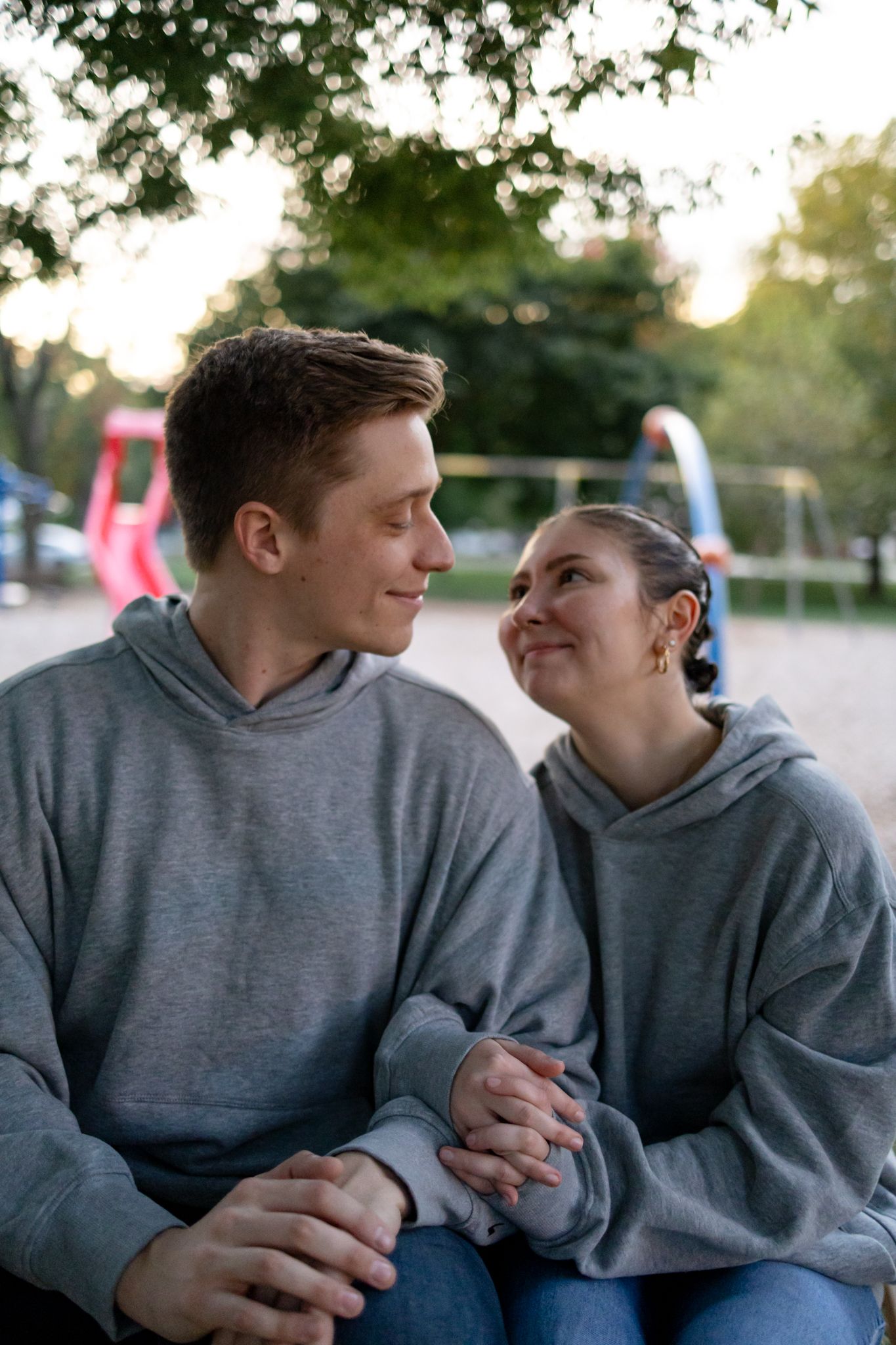 Two people in matching gray hoodies share laughter while sitting outdoors.