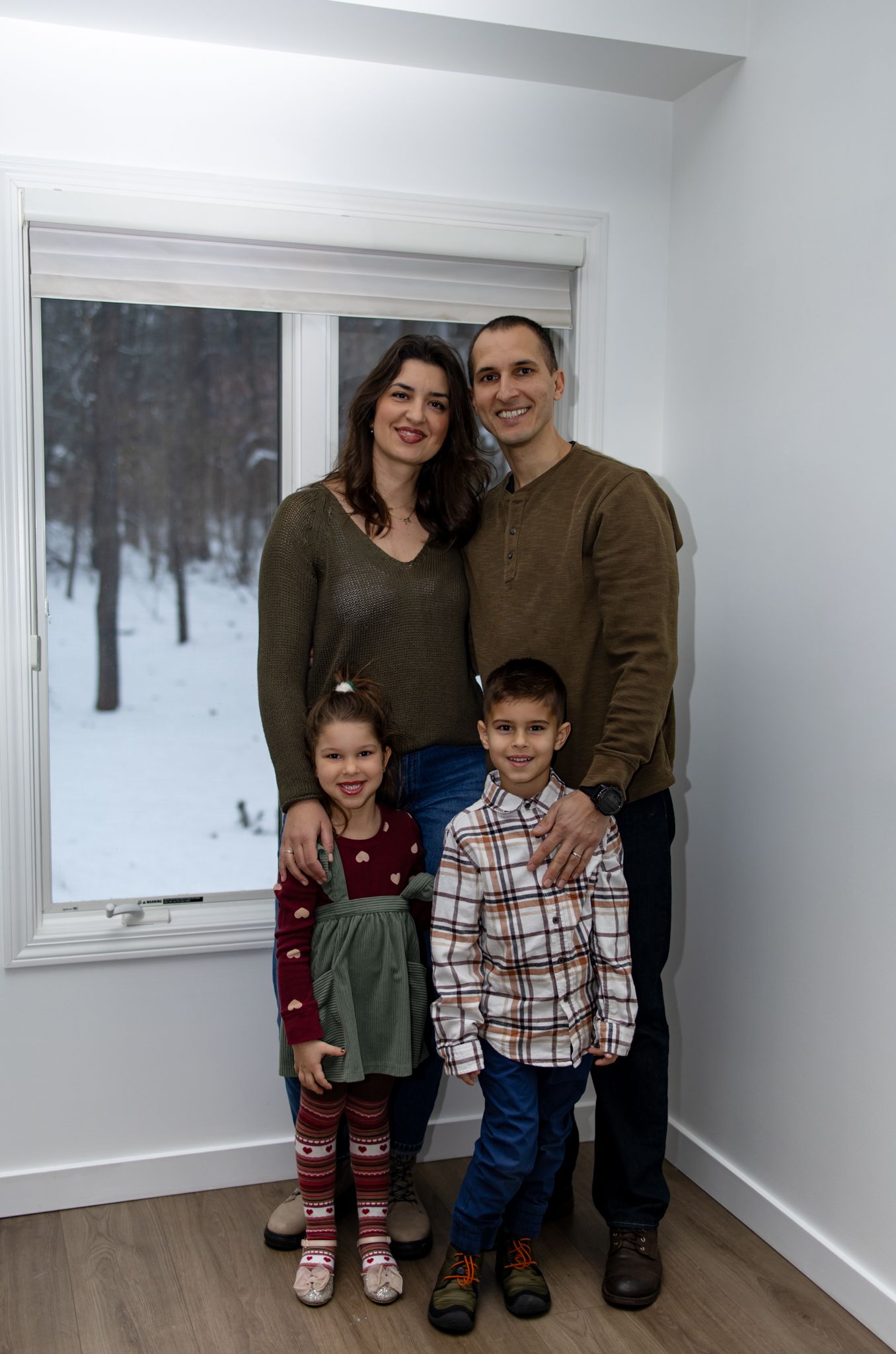 Indoor family portrait with snowy forest view through windows.