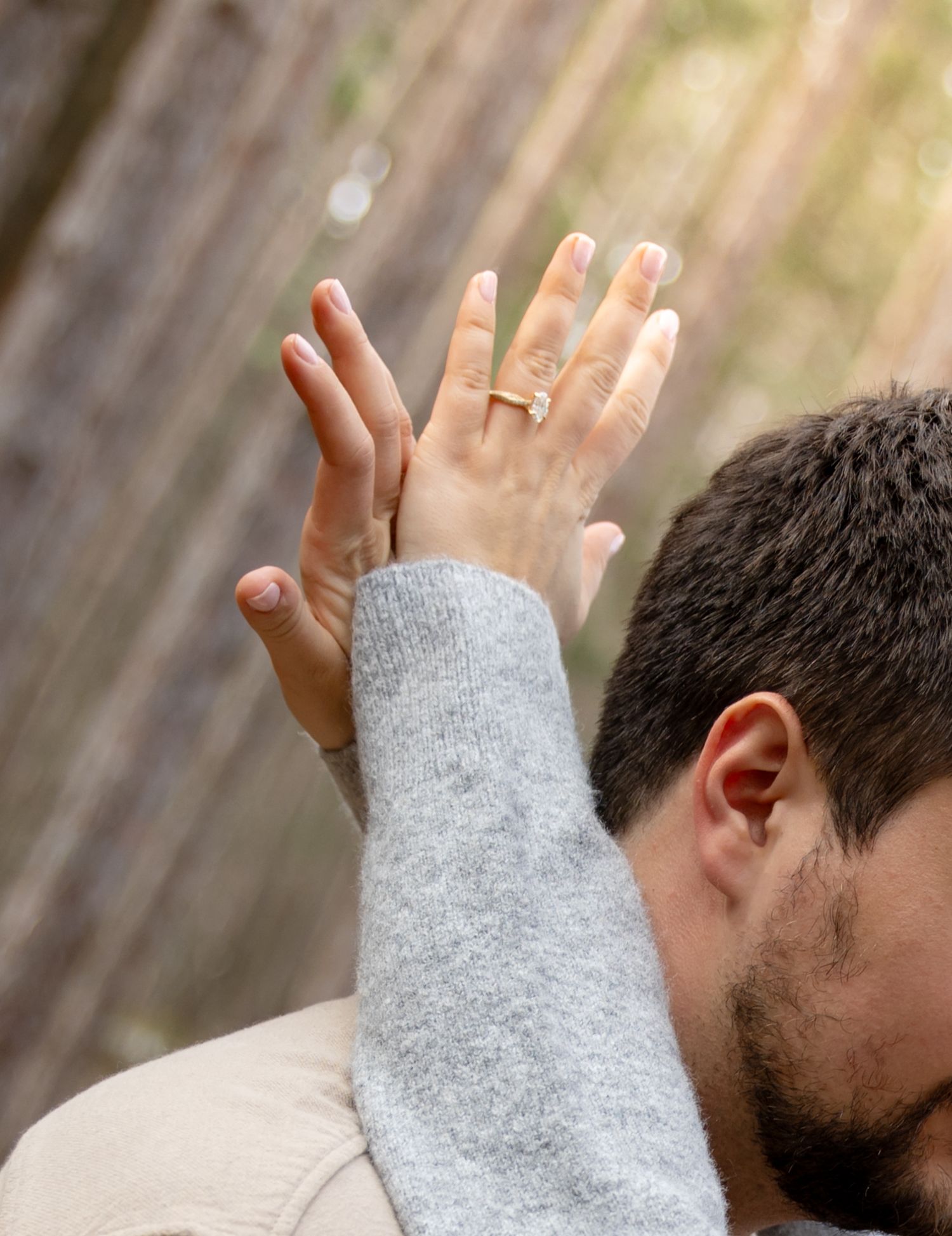 Close-up of a woman showing off her diamond engagement ring while embracing a man outdoors.