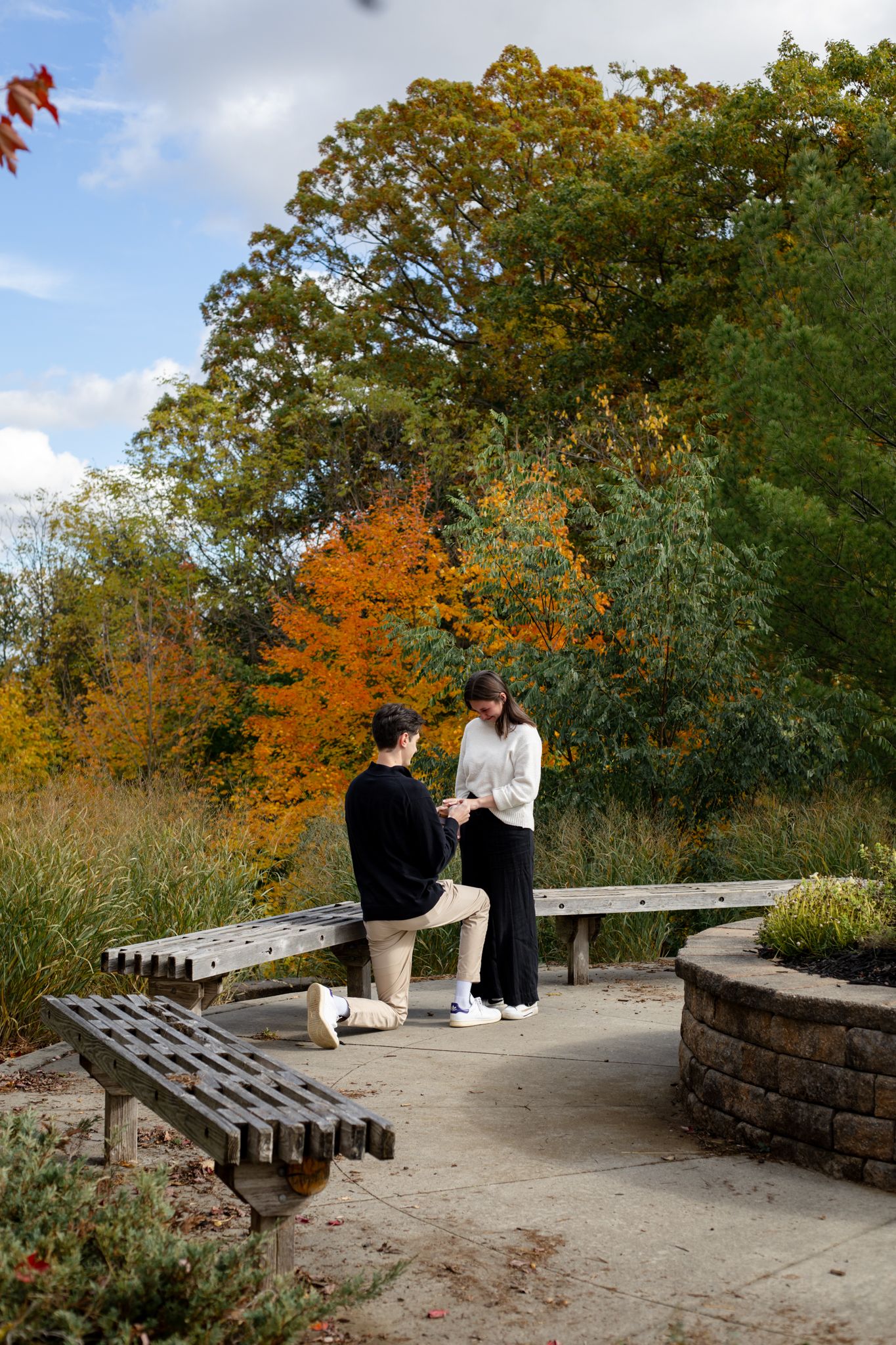 A romantic sequence on a stone bench surrounded by vibrant fall foliage.