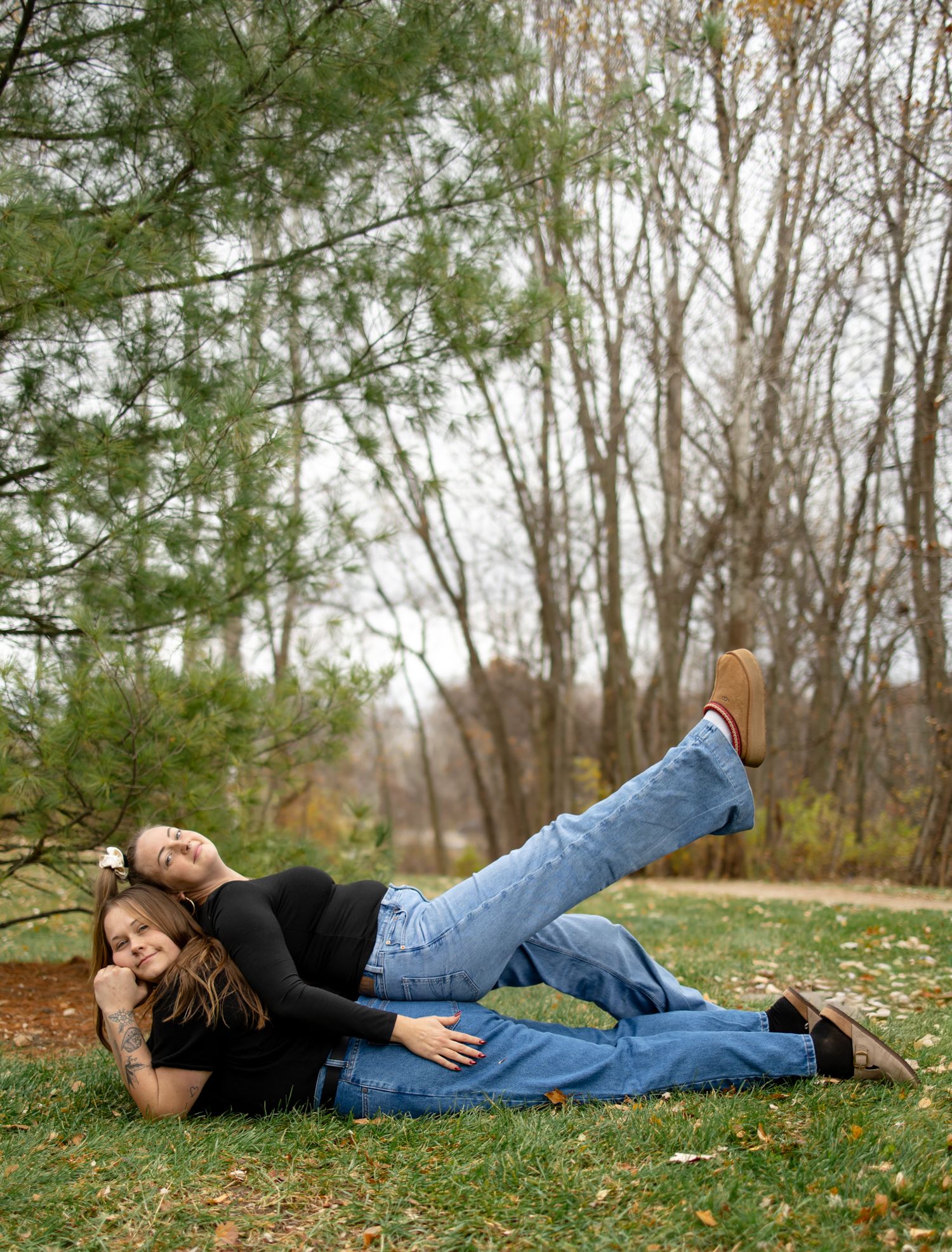 Person in black top and jeans lying on autumn grass among trees.