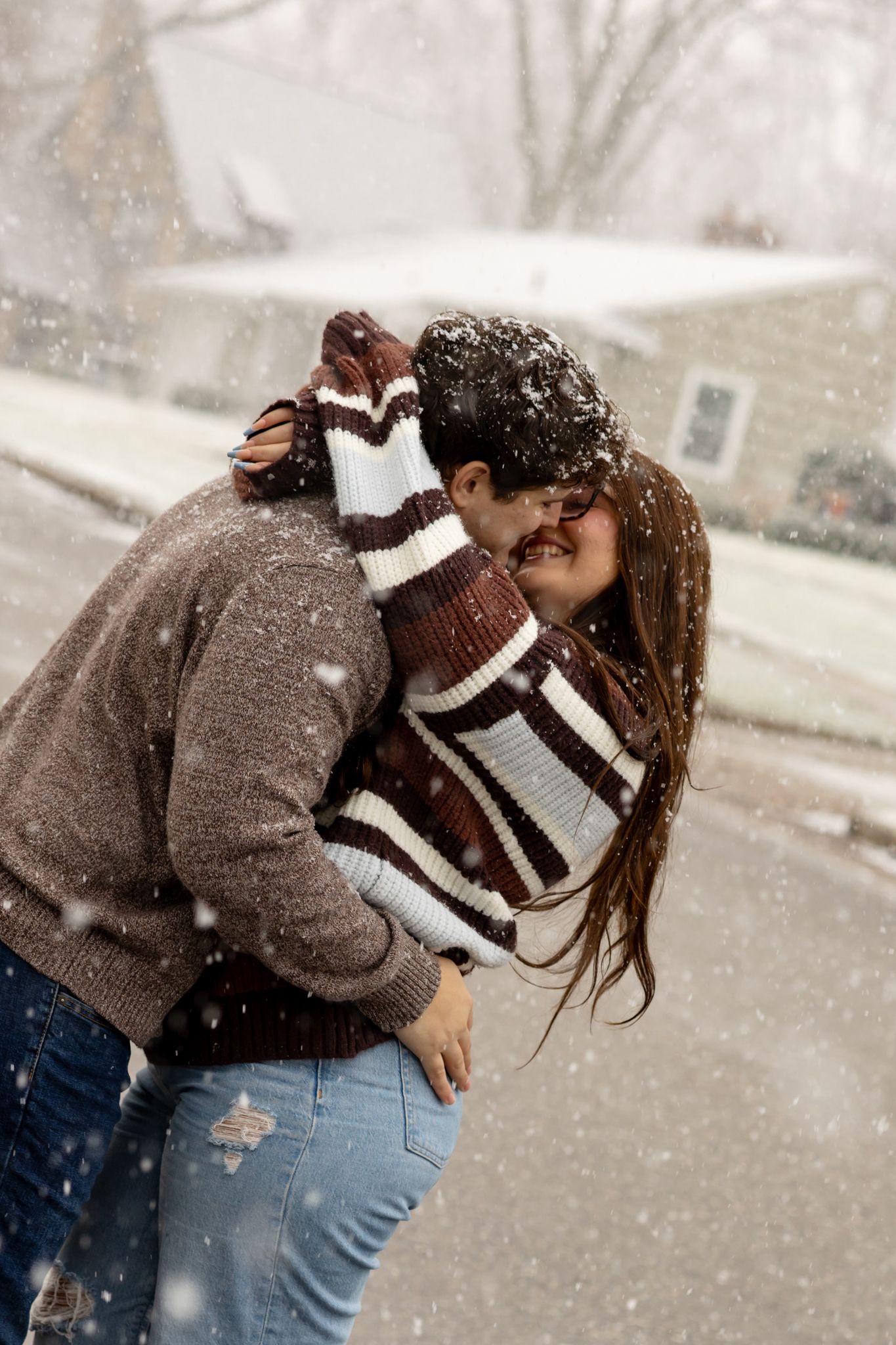 Couple sharing intimate moment during winter snowfall wearing cozy sweaters.