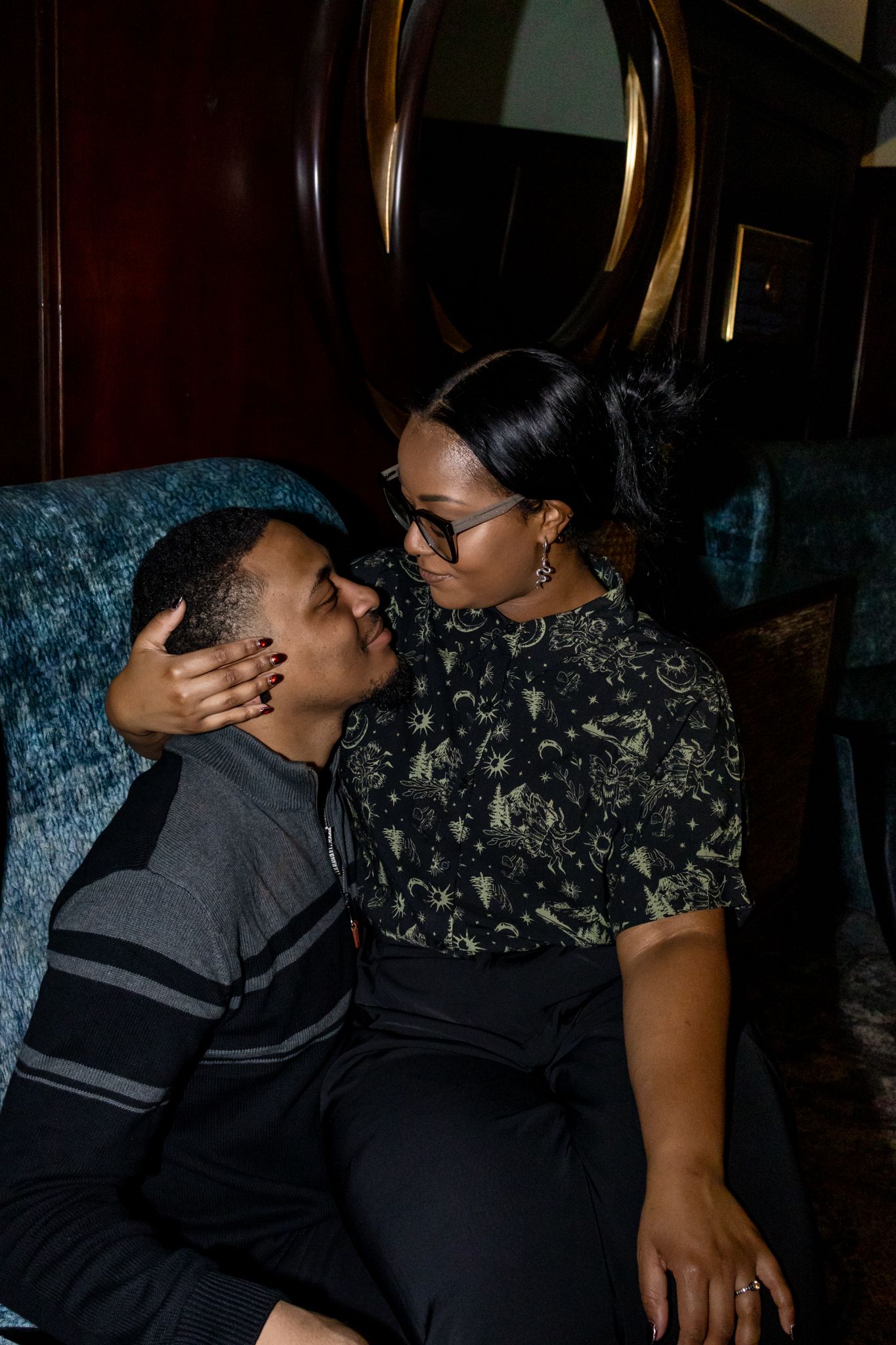 A couple shares an intimate kiss while wearing black and dark colored formal attire.