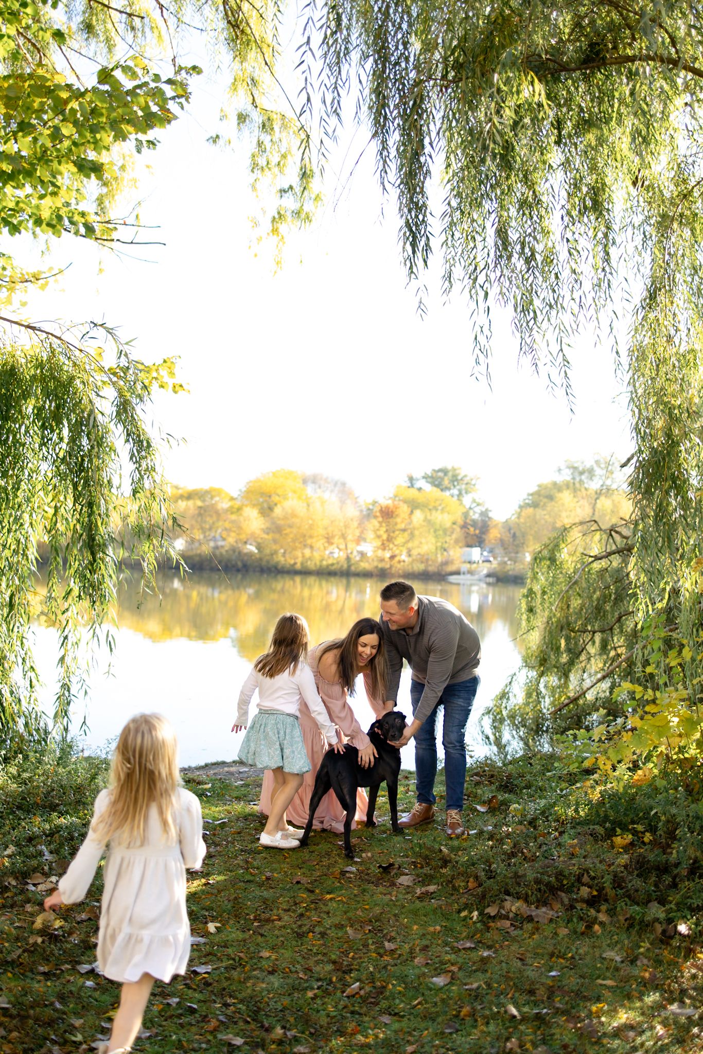 Family interacts playfully under willow trees during autumn photoshoot.