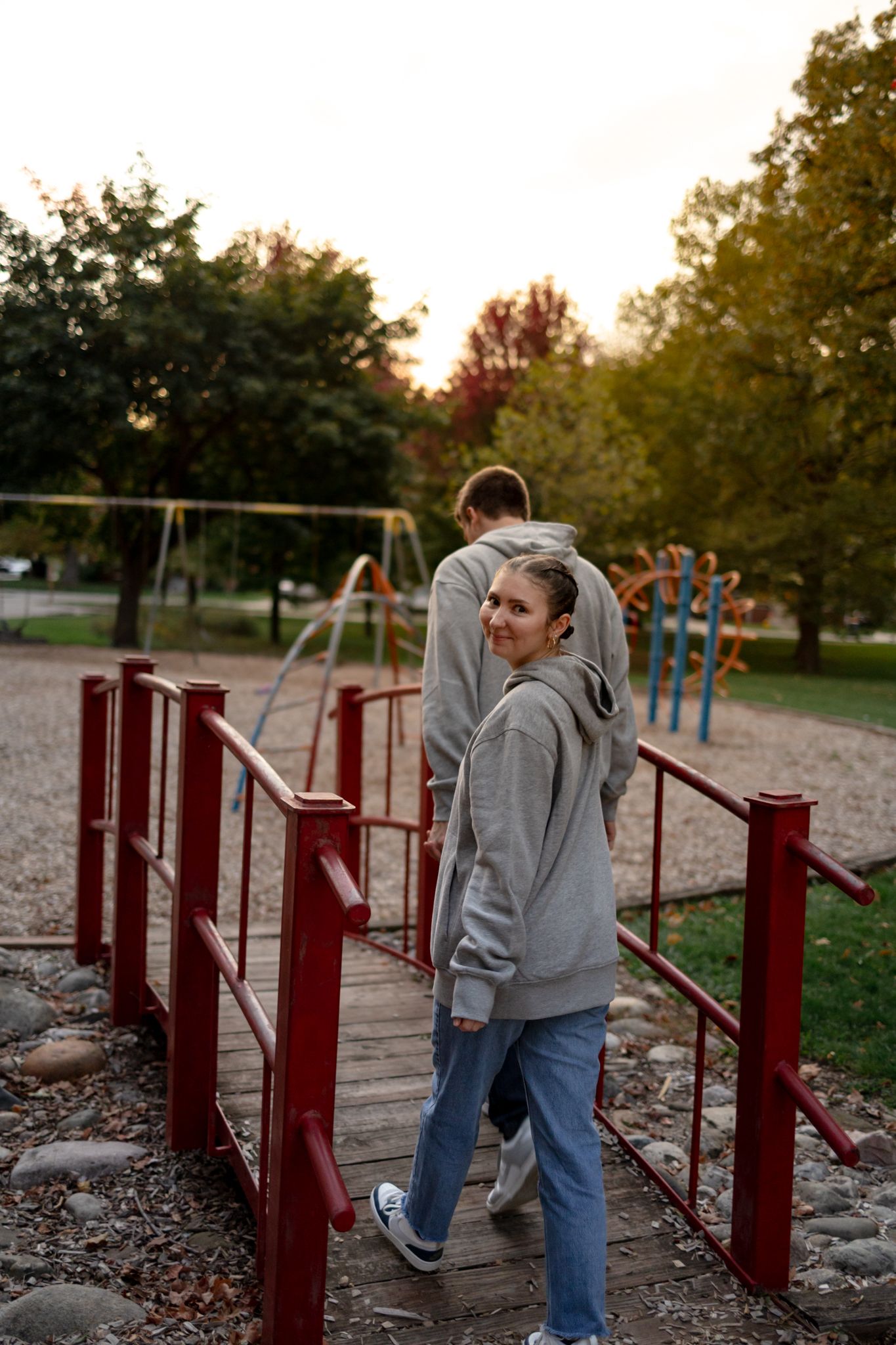 Two people in gray hoodies explore playground equipment at dusk.