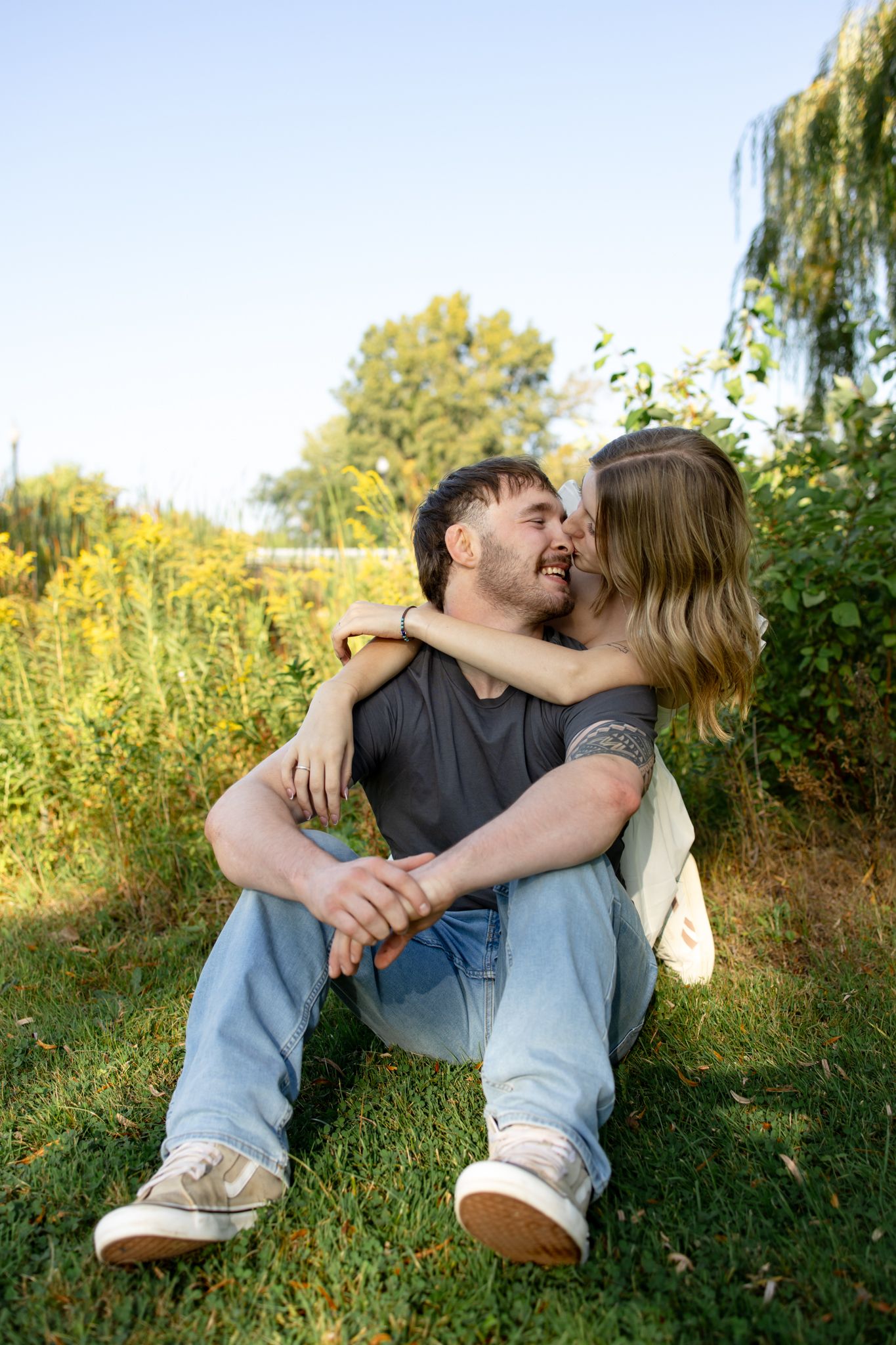 A couple sits together on grass sharing an intimate moment during sunset.
