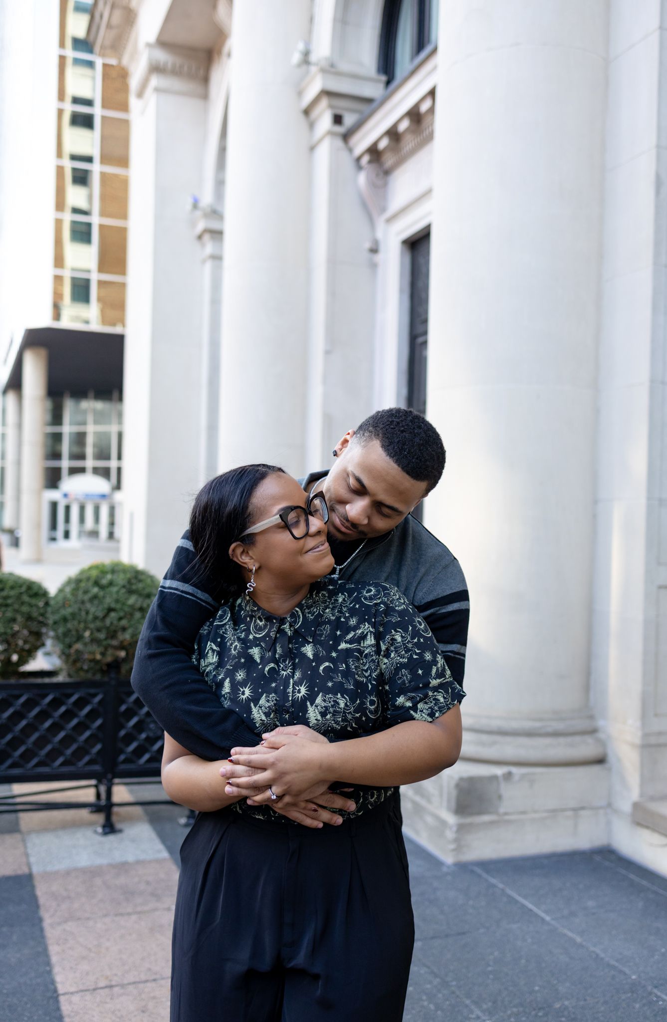 A couple shares a joyful embrace and laughter while posing in front of white columns of a grand building.