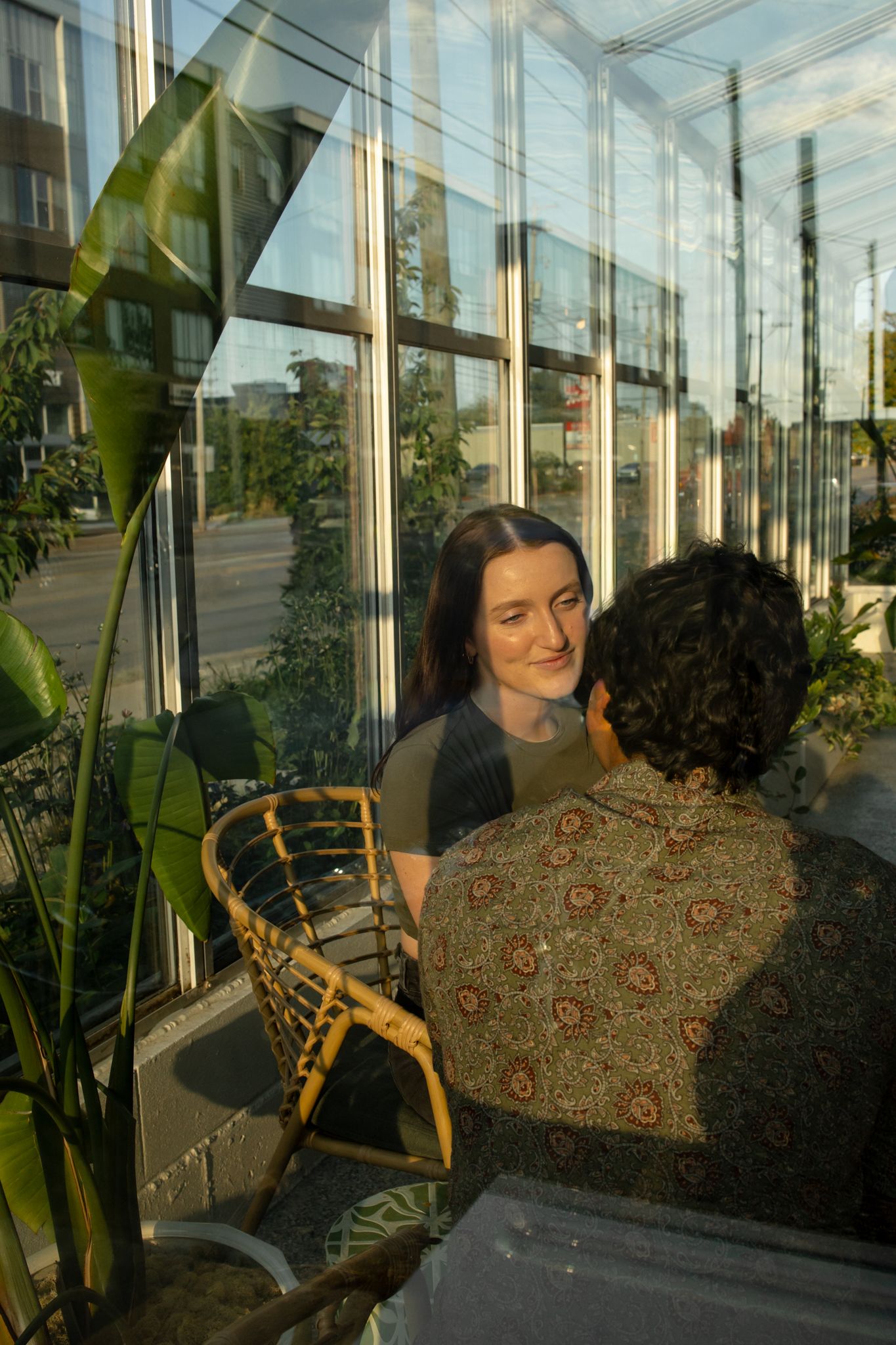 Couple shares intimate conversation by sunlit glass windows with indoor plants.