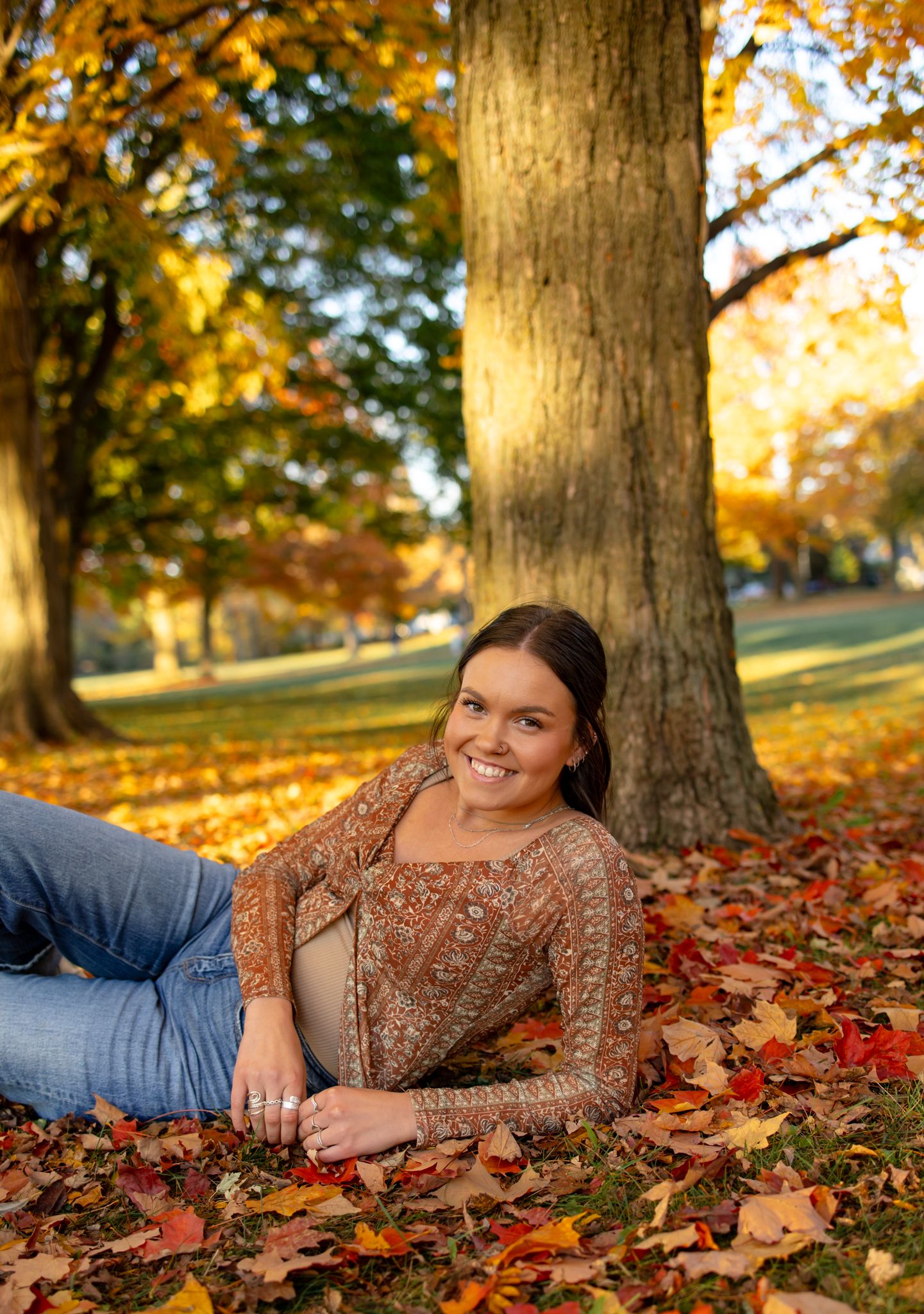 Person lying in fallen autumn leaves wearing brown patterned top and jeans.