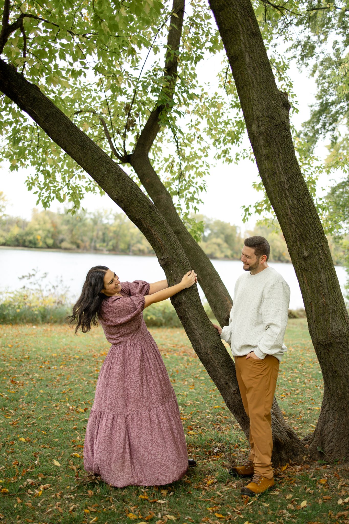 Two people pose playfully under autumn trees wearing coordinated casual outfits.