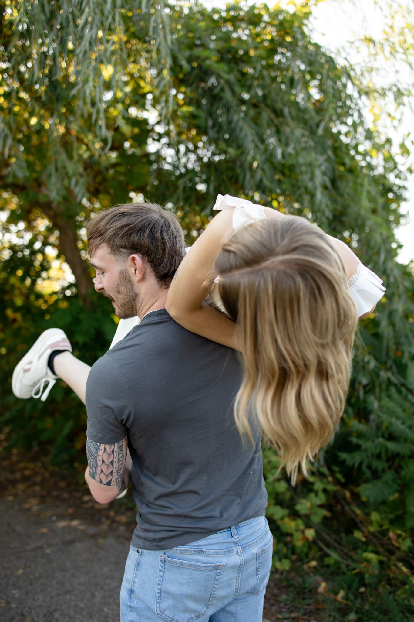 A couple embraces while spinning in front of autumn trees during golden hour.