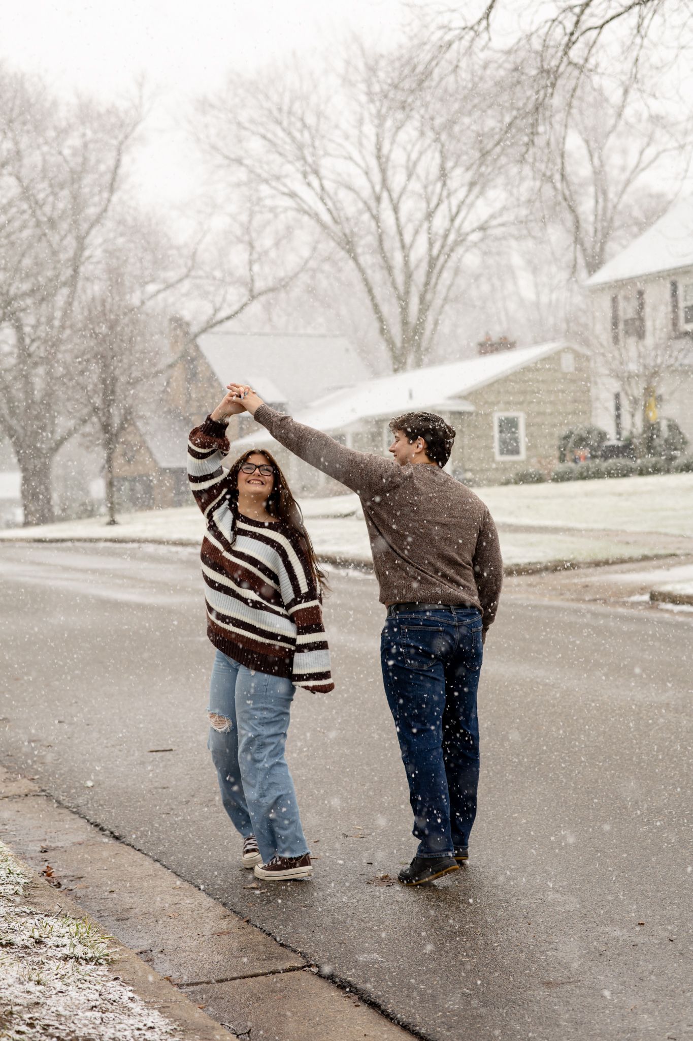 A couple dancing playfully in the snow on a winter street.