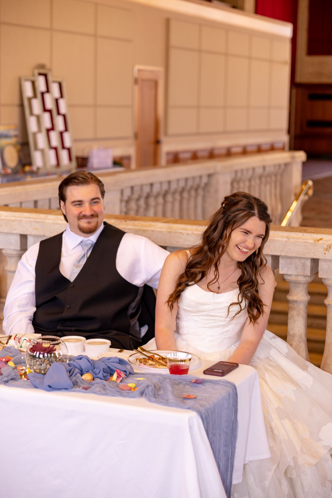 Happy bride and groom smiling at sweetheart table during wedding reception in elegant ballroom venue.