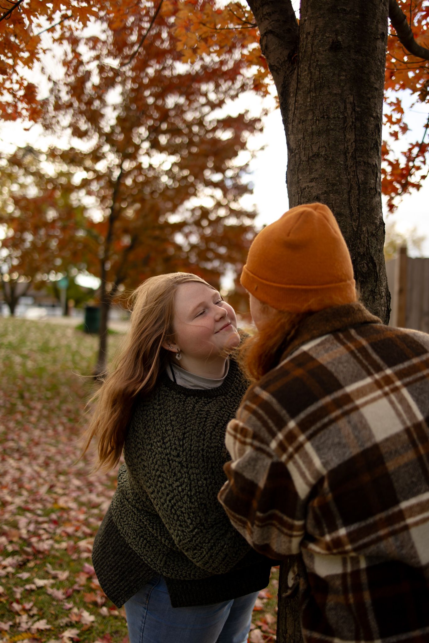 A couple in cozy fall sweaters and plaid share an intimate moment under autumn trees.