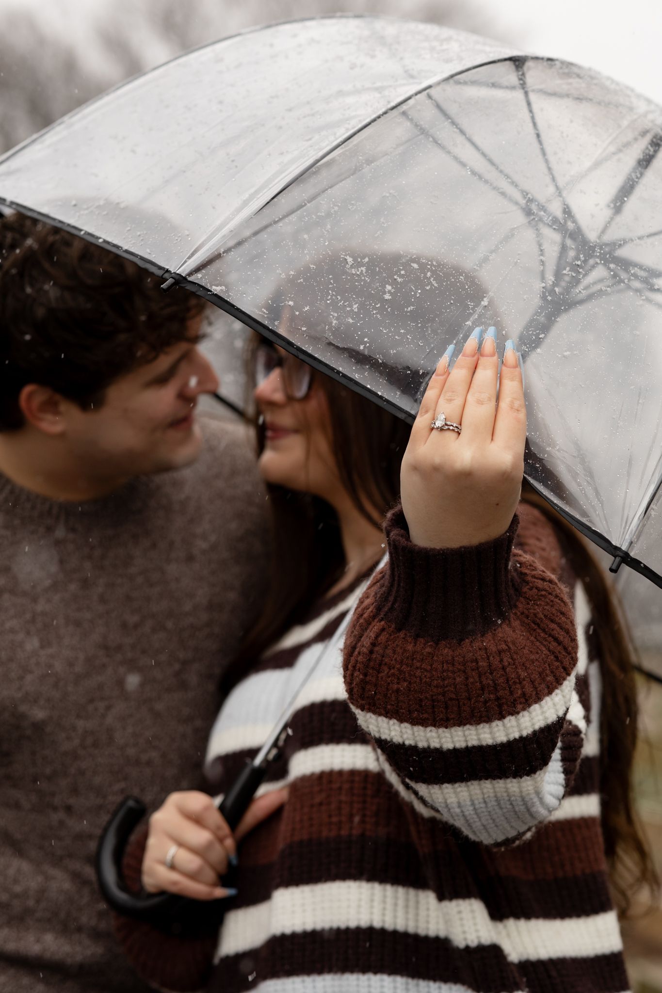 Two people sharing an intimate moment beneath a transparent umbrella in the snow.
