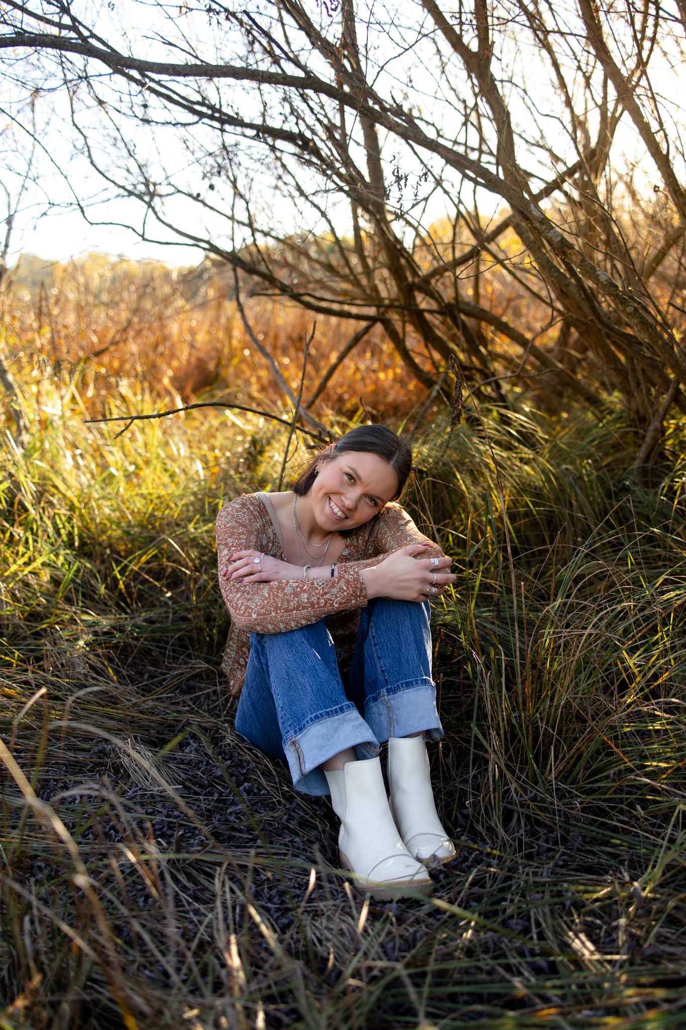 Person sitting in tall grass during golden hour wearing a sweater and jeans.