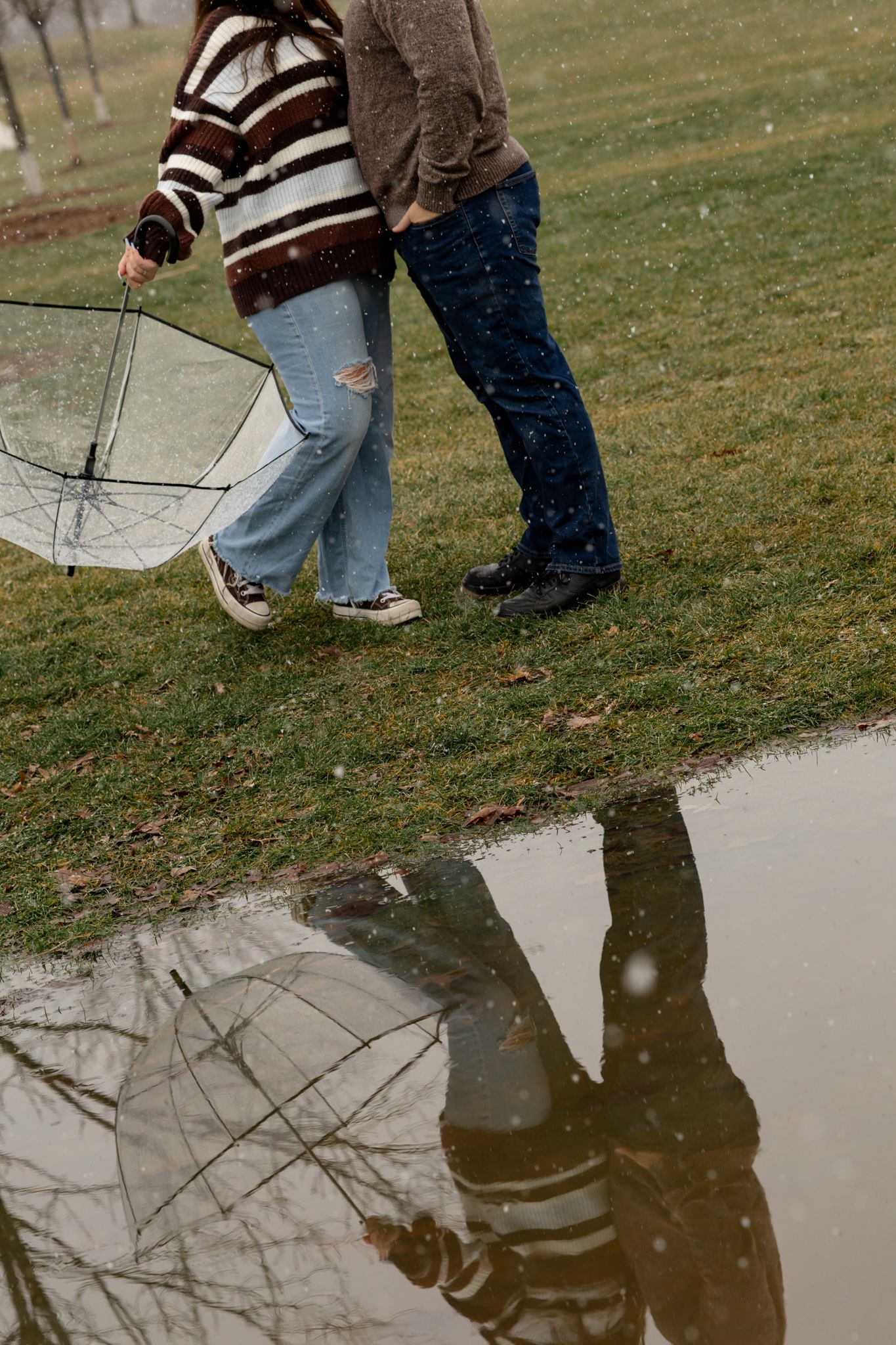 Reflections in a puddle show two people with an umbrella on a winter day.