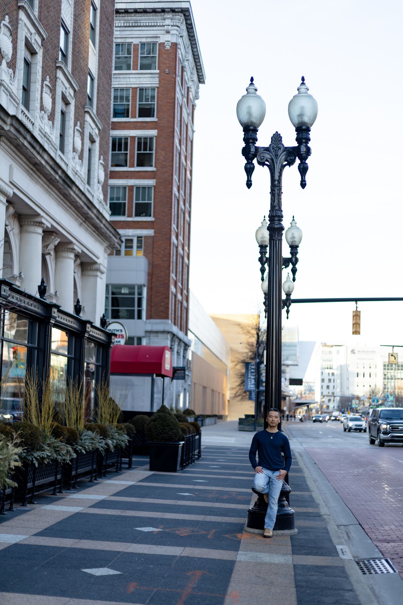 A series of vintage-style street lamps line an urban sidewalk with brick buildings and storefronts in the background.