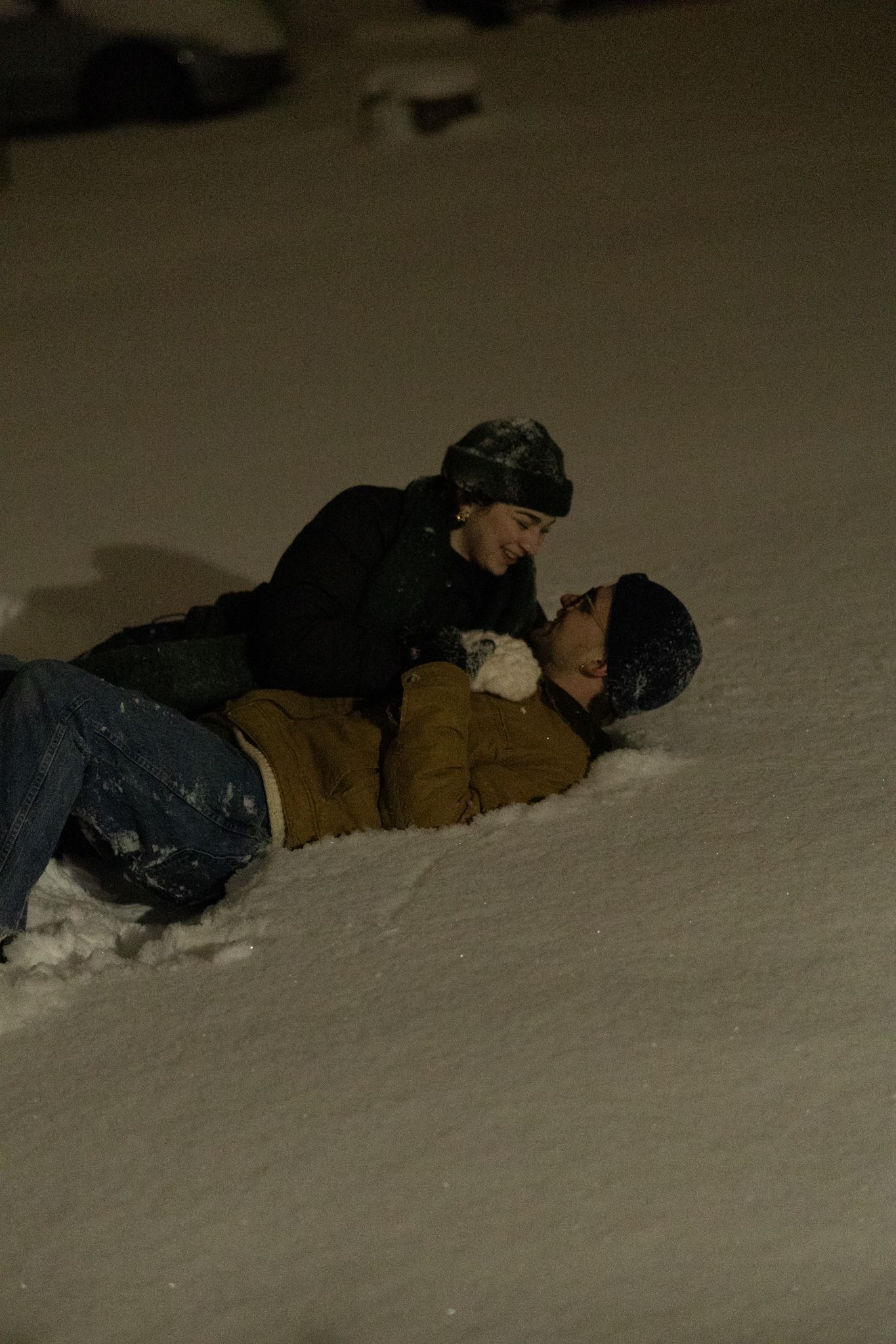 Two people lying in deep snow at night.