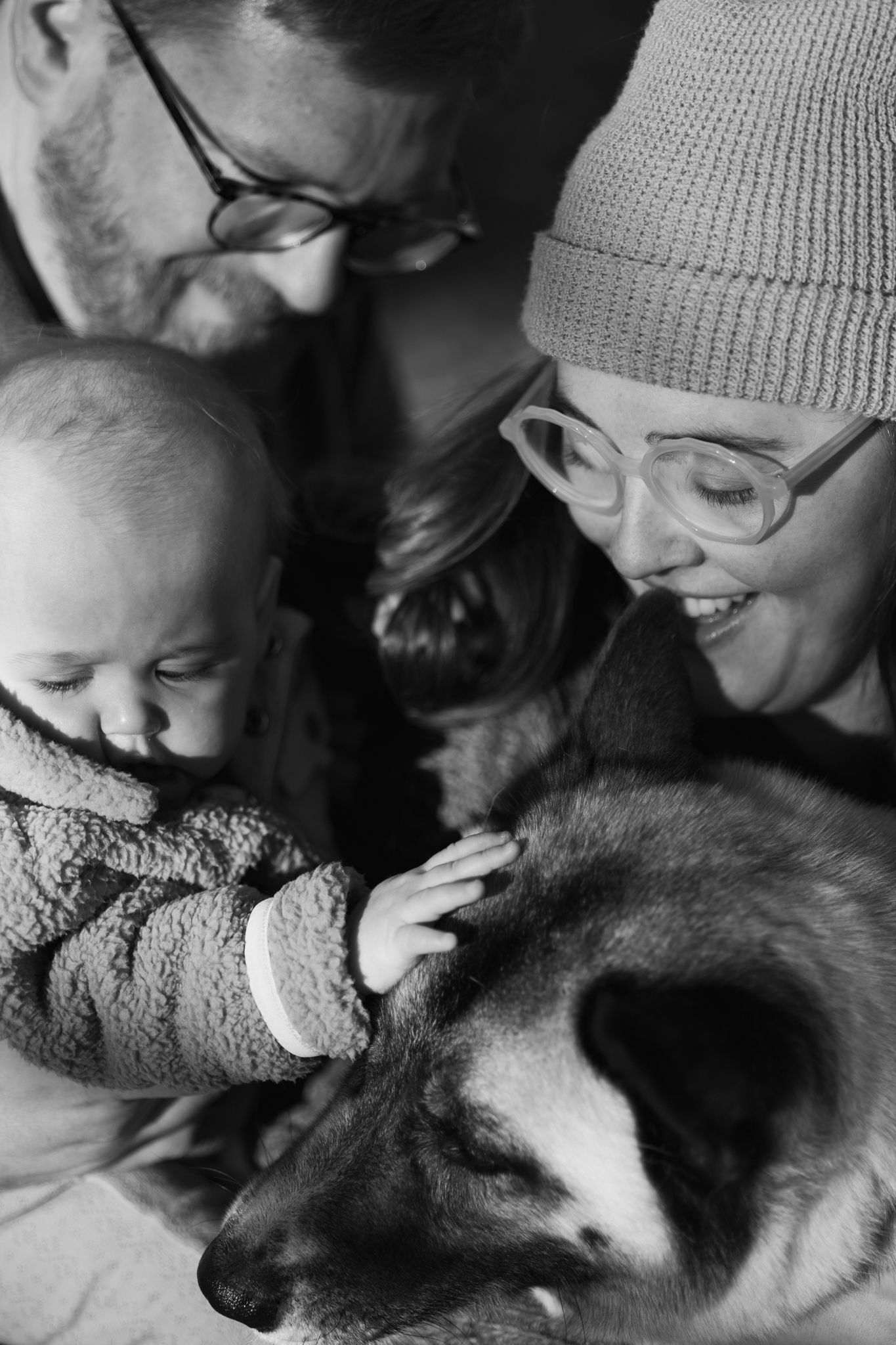 An intimate black and white portrait of a family bonding with their husky dog.