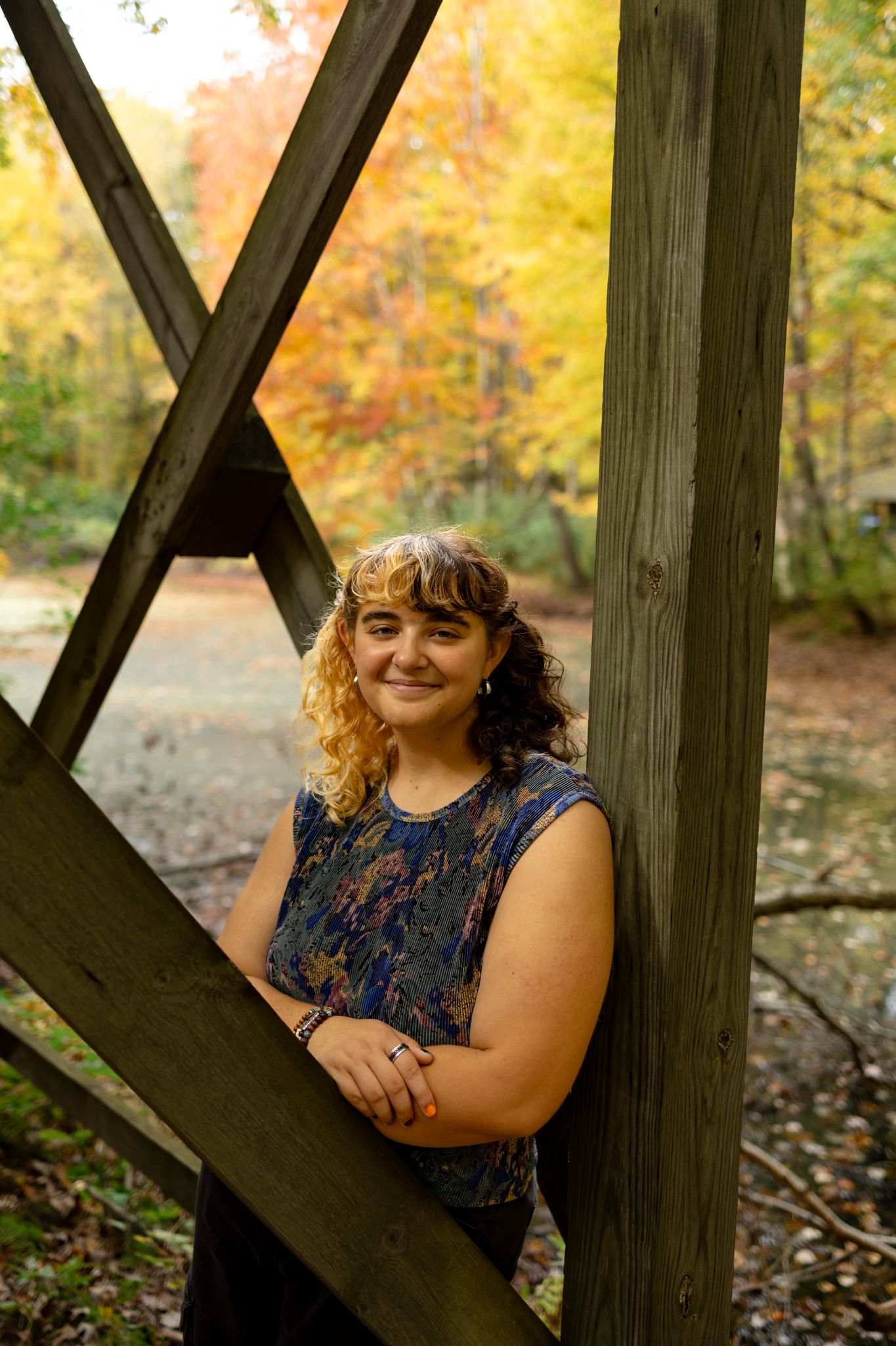 A person poses against wooden beams with fall colors in the background.