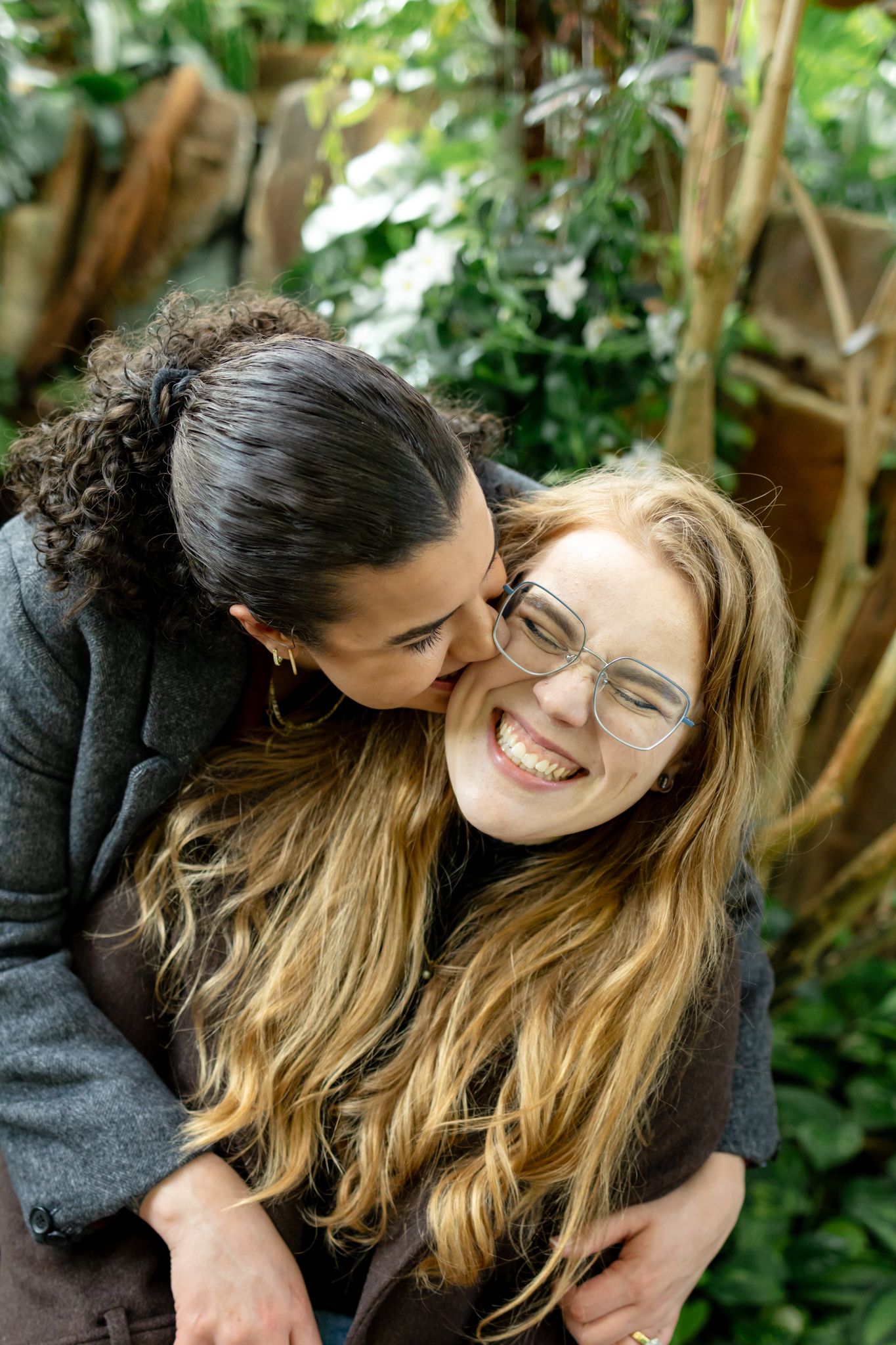 Two people sharing a joyful moment together outdoors with greenery in the background.