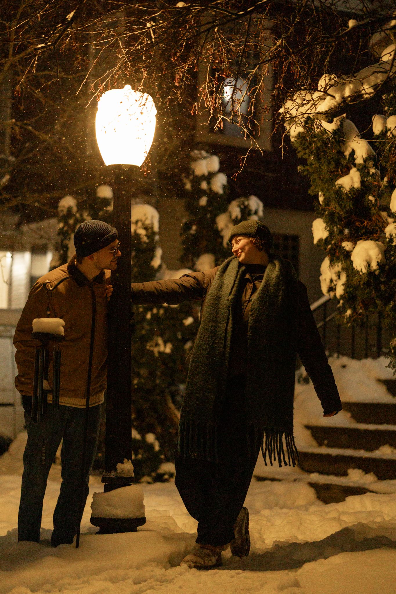 A couple sharing a winter evening moment under snow-covered trees and lamplight.