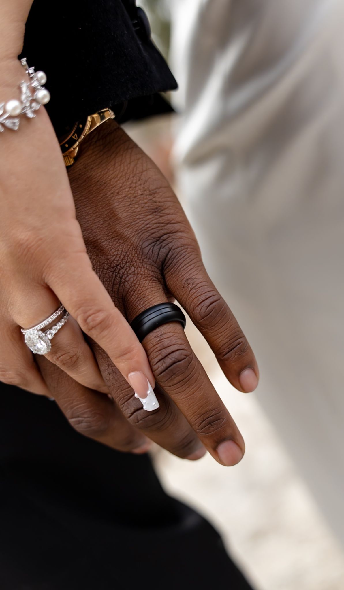 Close-up of an interracial couple holding hands, displaying wedding rings and bracelets.