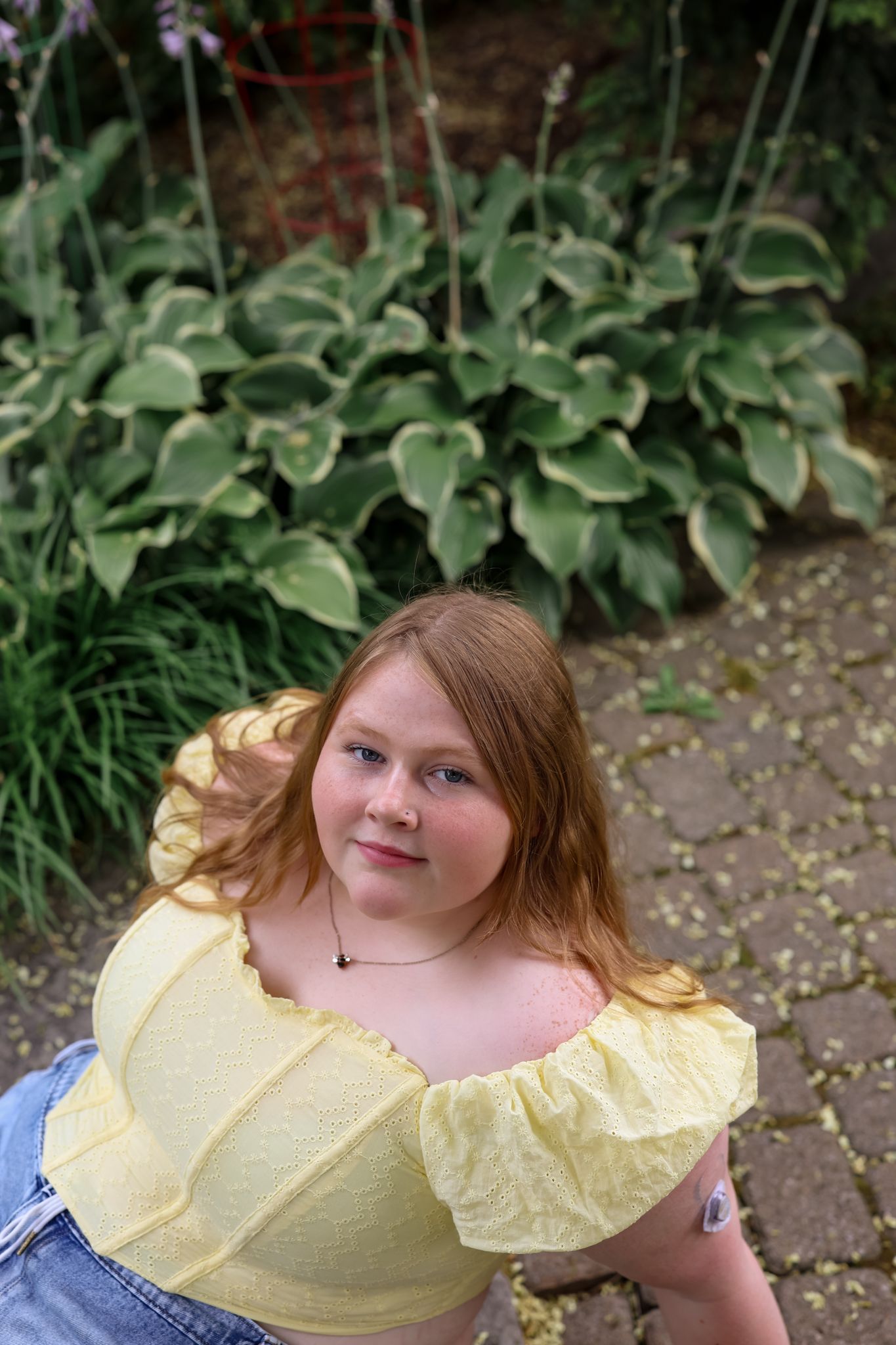 Person in yellow ruffled top posing against garden greenery background.