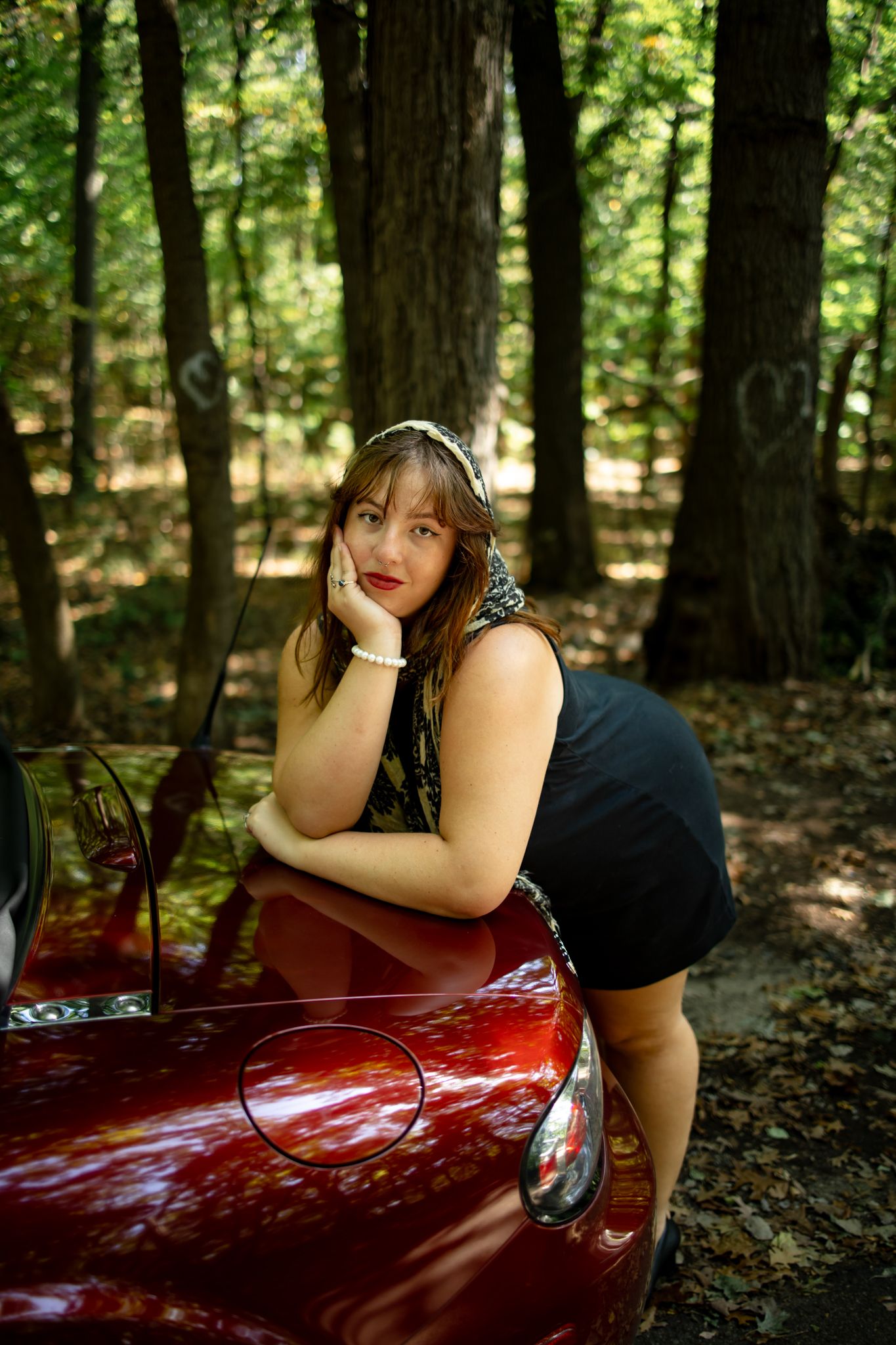 Red sports car photoshoot in wooded forest setting with dramatic lighting.
