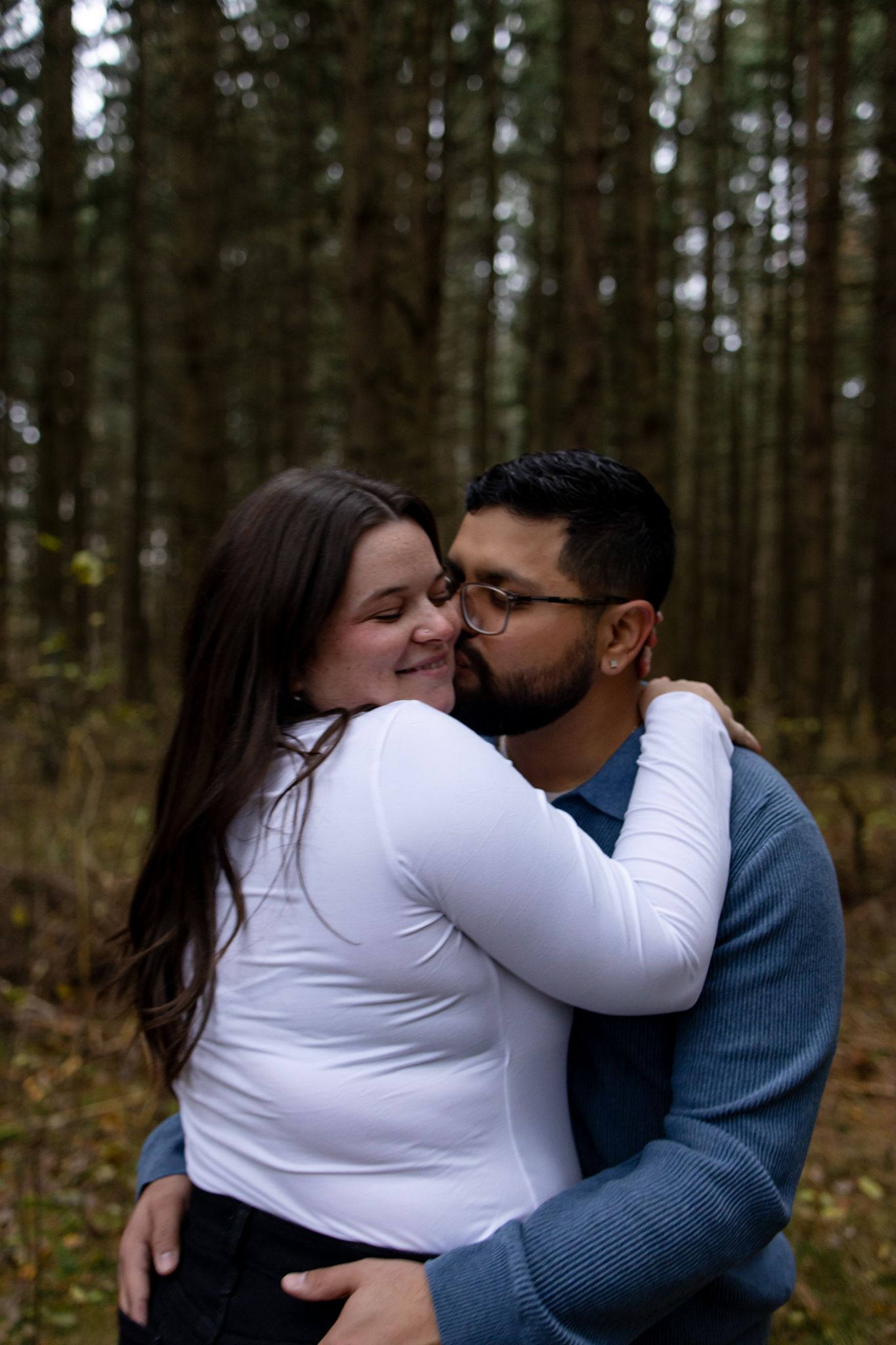 Intimate embrace between couple in a forest setting wearing contrasting white and blue sweaters.