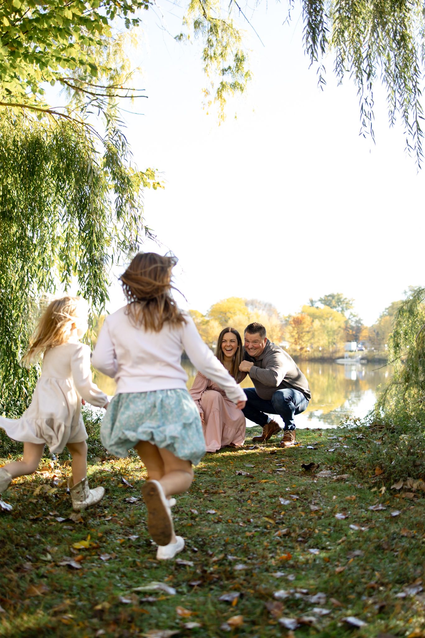 Family members run and play on grass covered hill by the lake.