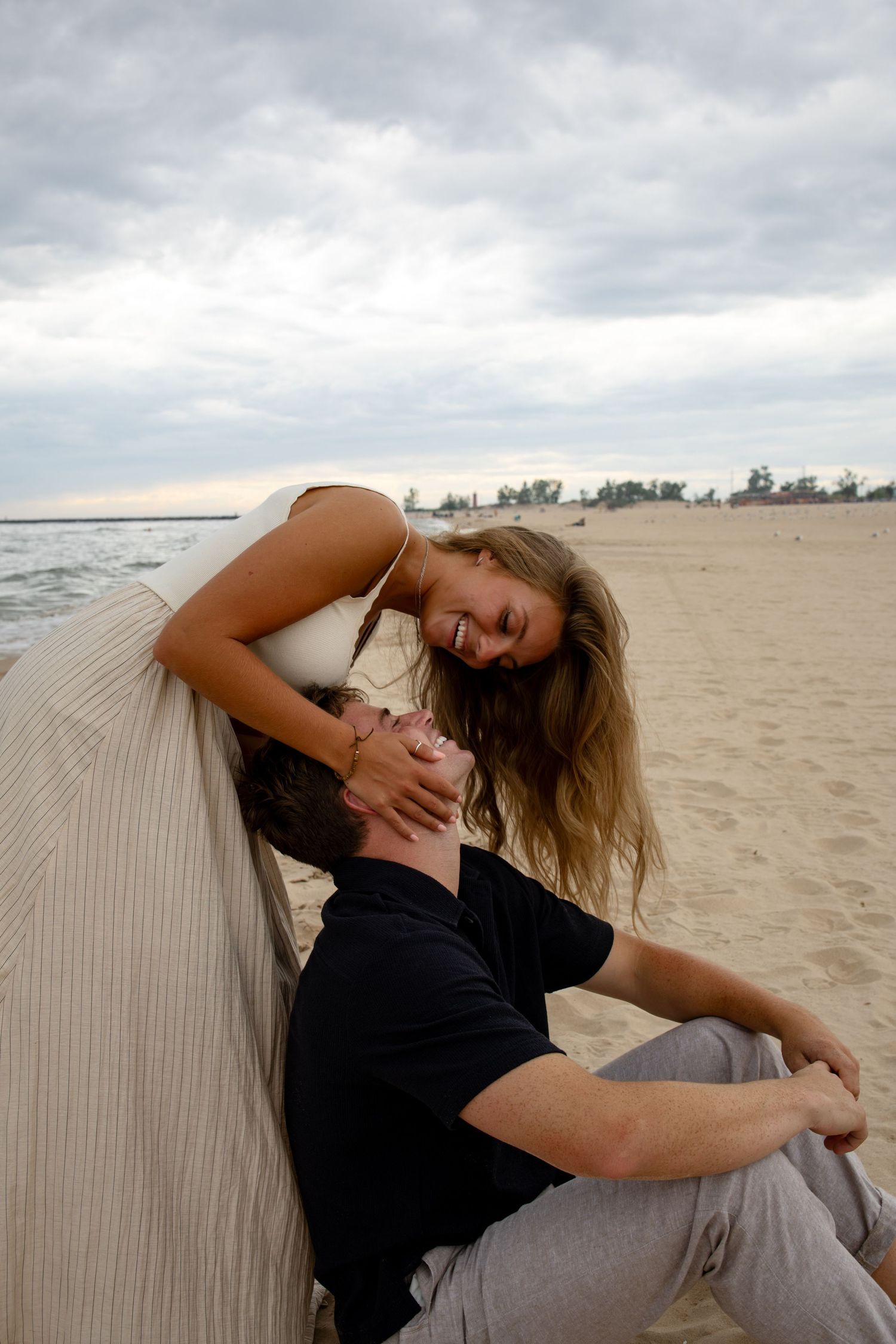 Couple sharing an intimate moment on a sandy beach under cloudy skies.