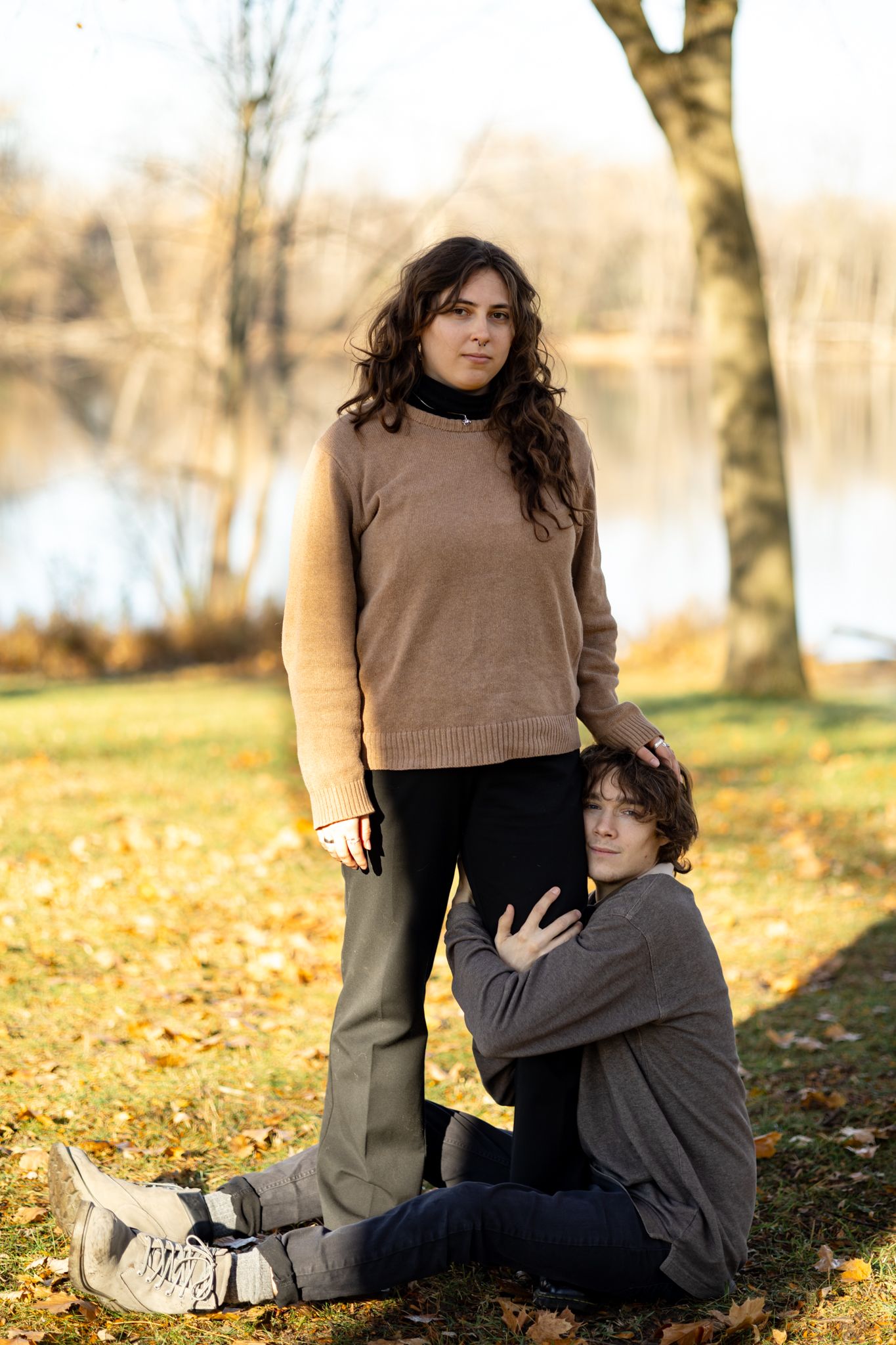 Two people sharing intimate moments while sitting on fallen autumn leaves by a lake.