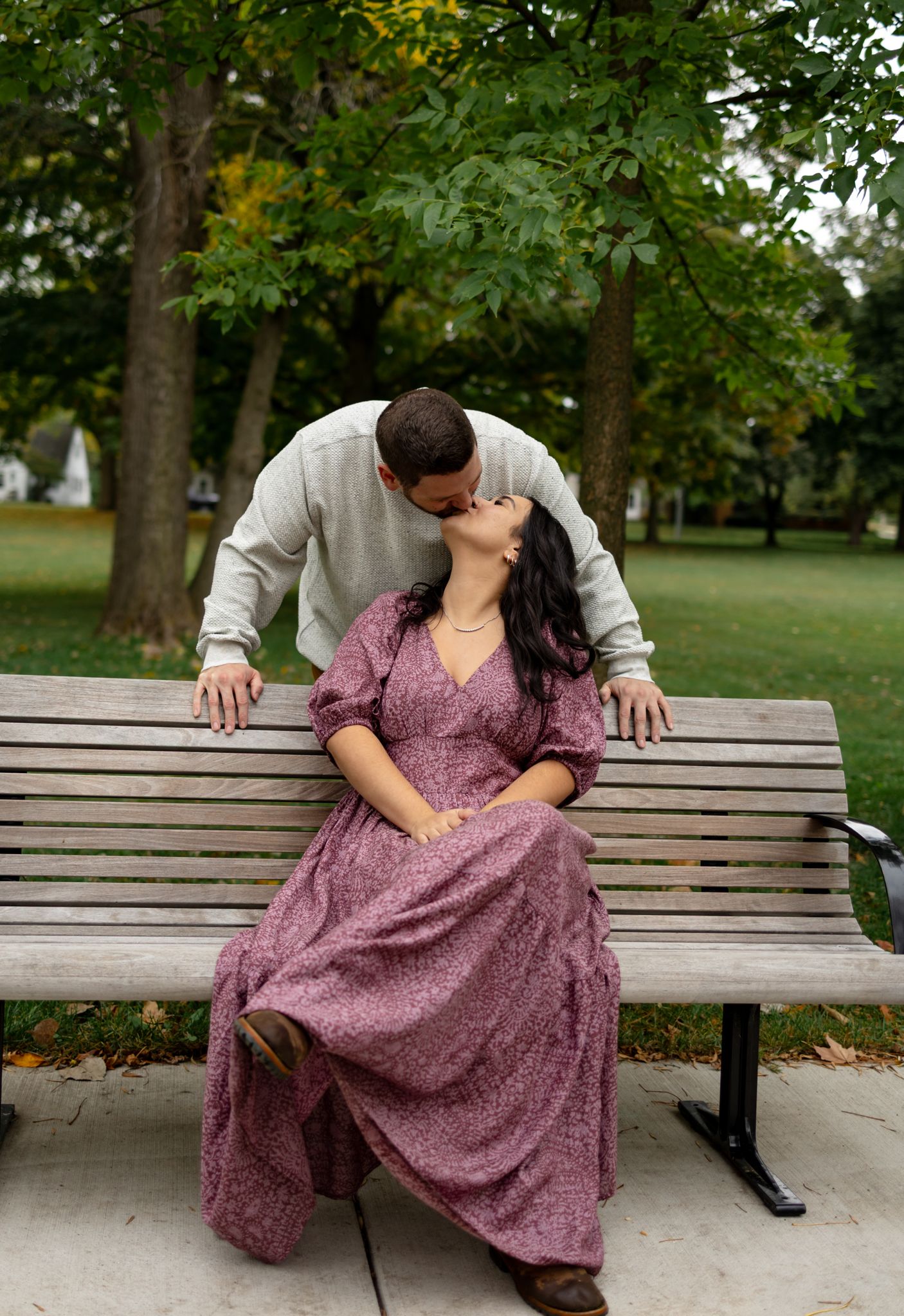 Two people sit together on a wooden park bench in coordinated fall outfits.