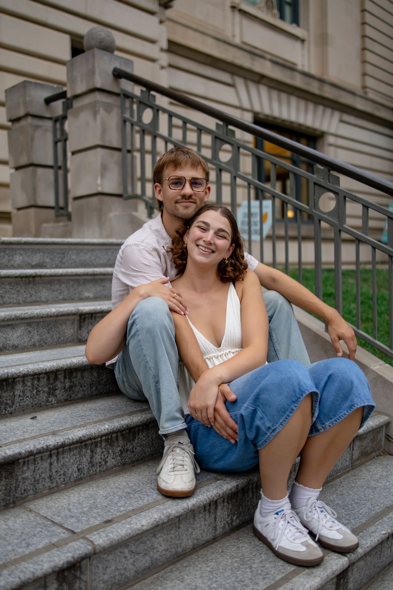 Candid moment of couple relaxing on concrete steps in casual summer attire.