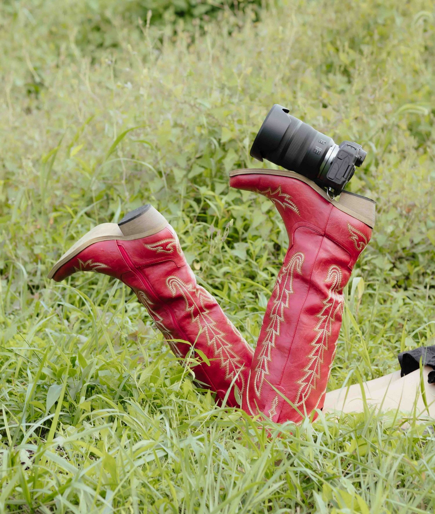 Red cowboy boots with gold embroidery standing upright in grass with a camera balanced on top.
