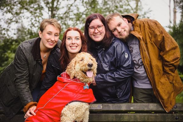 Happy goldendoodle in red jacket enjoys outdoor time with companions.