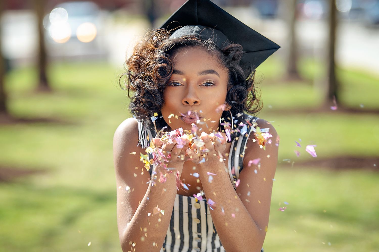 african american female graduate student blowing confetti wearing a graduation cap with a tassel