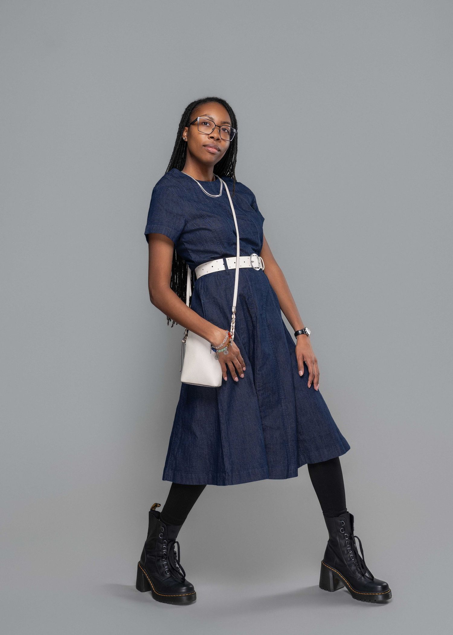 African American female 29th birthday studio photo session; leaning wearing a blue dress with white belt and a white crossbody purse.