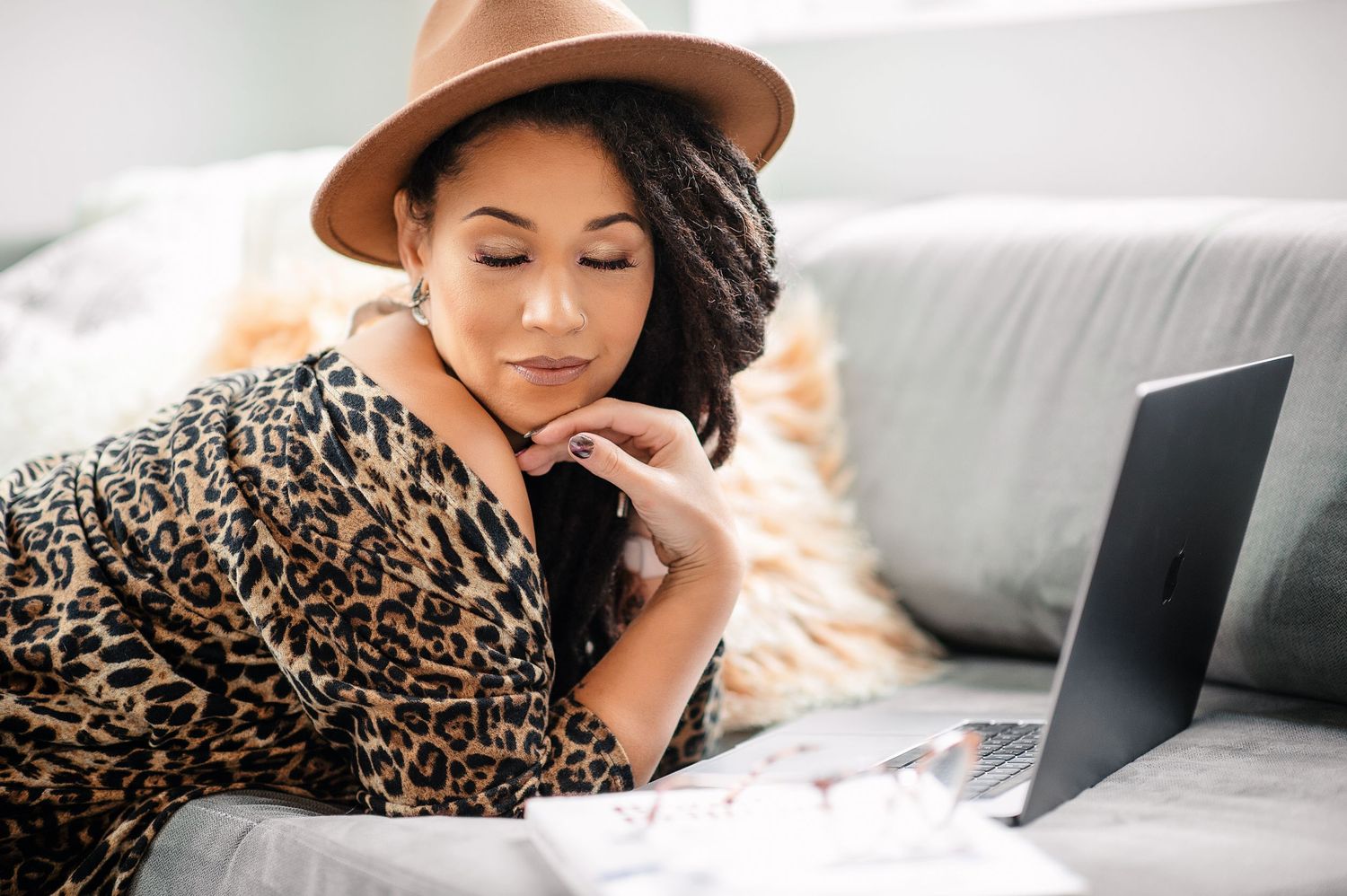 African american female wearing a hat, laying on a sofa with laptop and eyes closed.